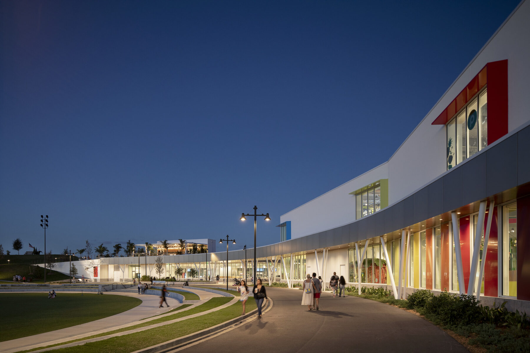 pedestrians walking across the colorful facade of the Children's Museum lit up at night.