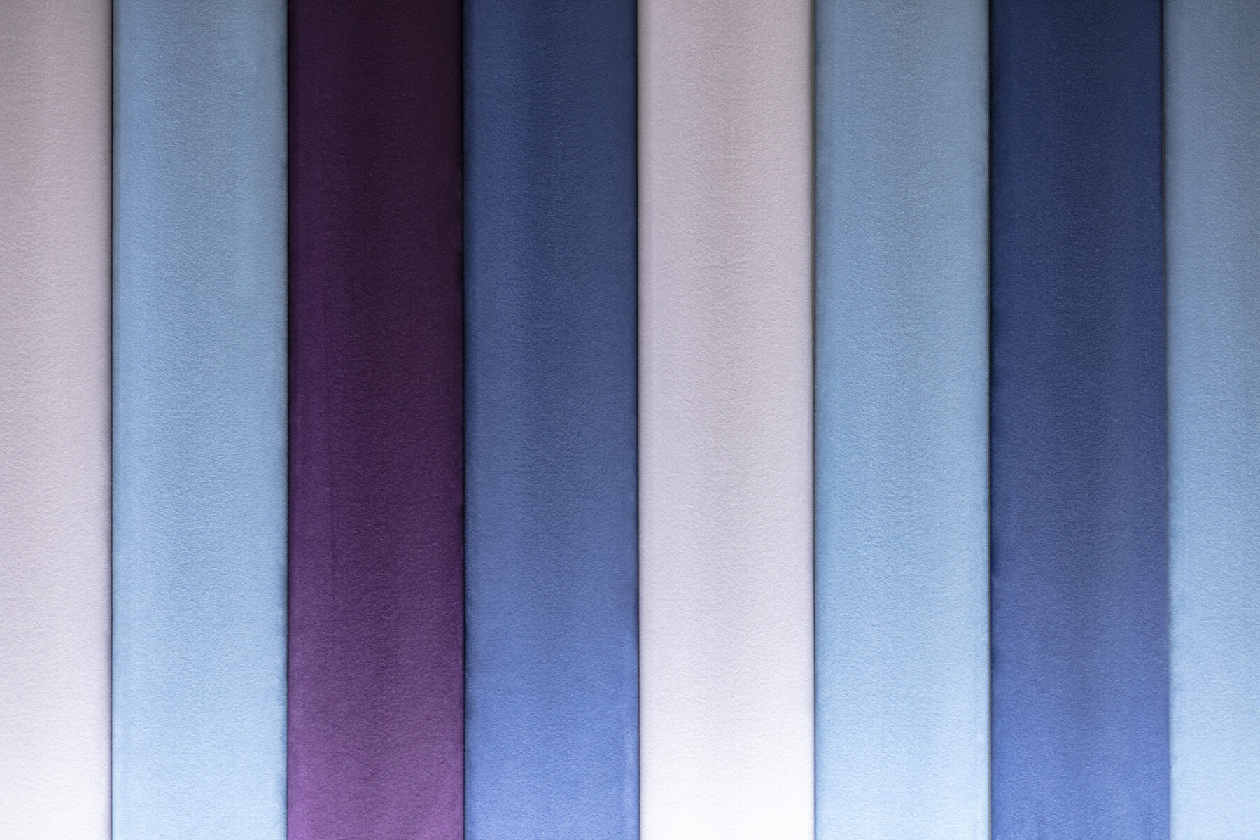 a close-up shot of the wall's upholstered stripes. the stripes are varying shades of blue and purple.