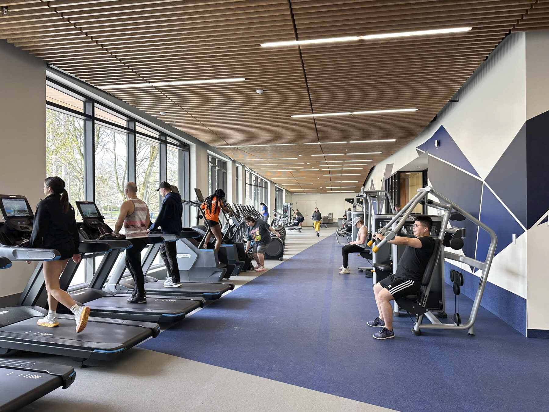 brightly lit room with students exercising on treadmills, weight machines, and other workout equipment