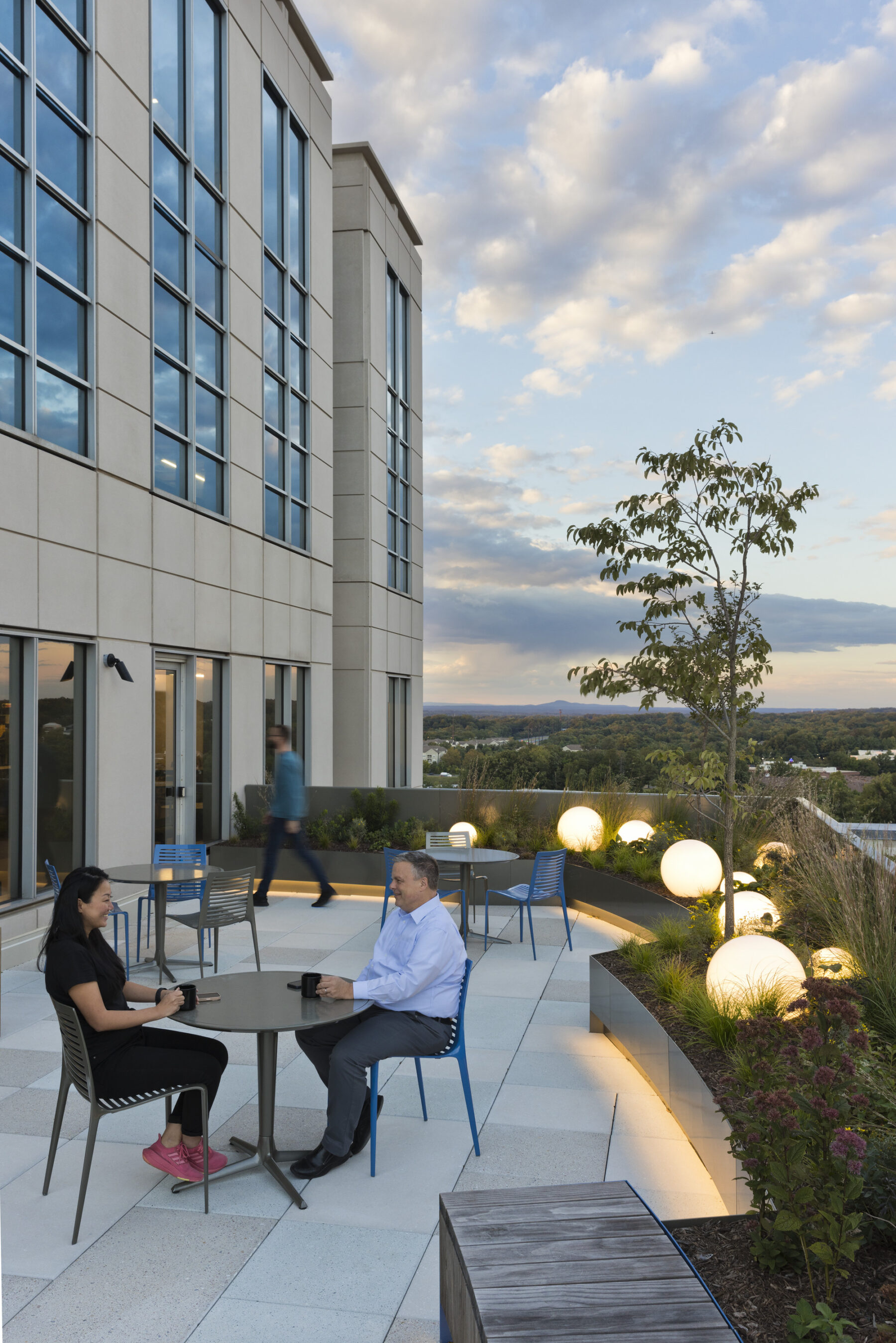 Roof terrace from exterior at dusk with individuals sitting at table with orb lights in the background