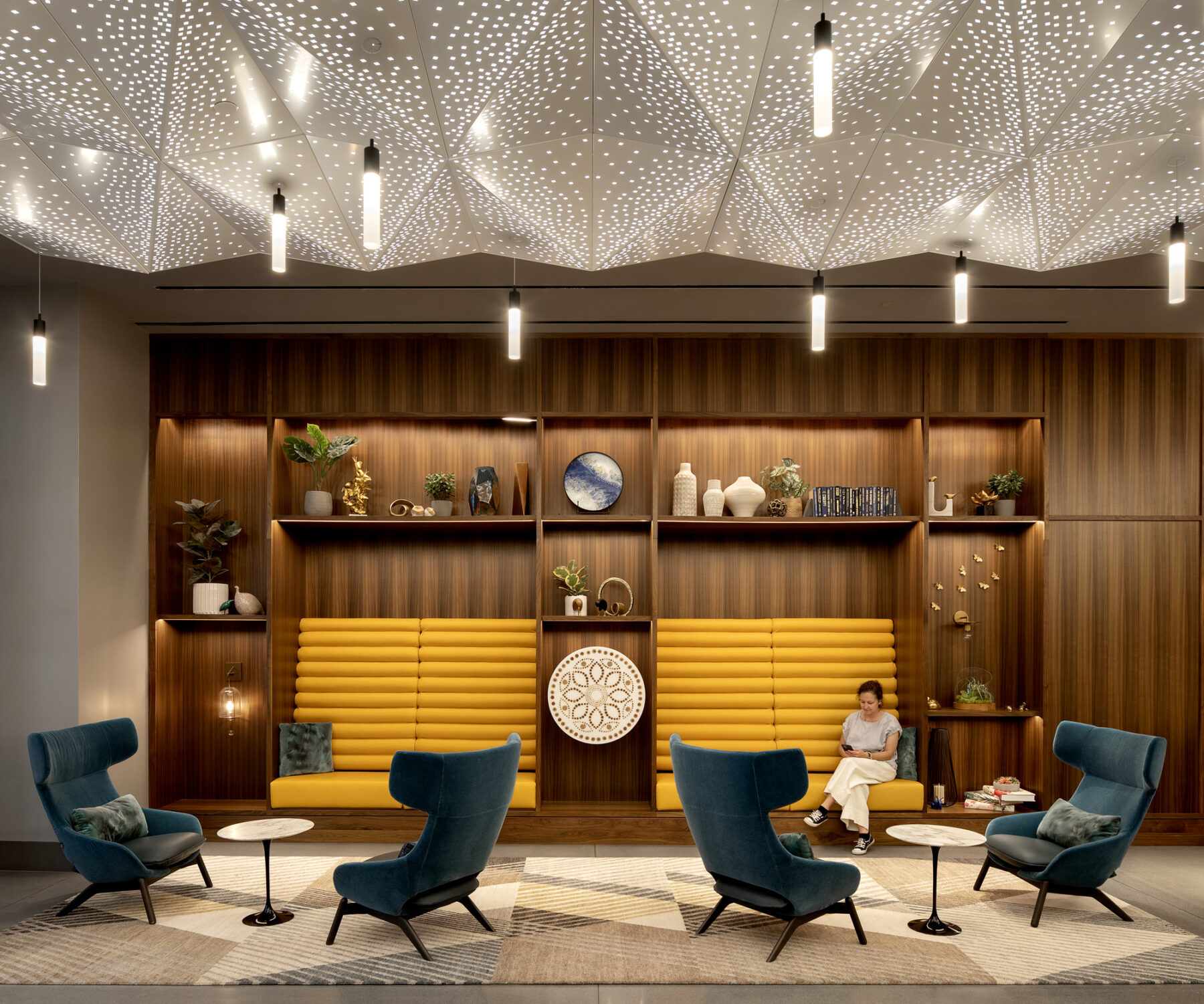 photograph of interior lobby space with backlit perforated ceilings, a millwork with curated decorations, and custom furniture
