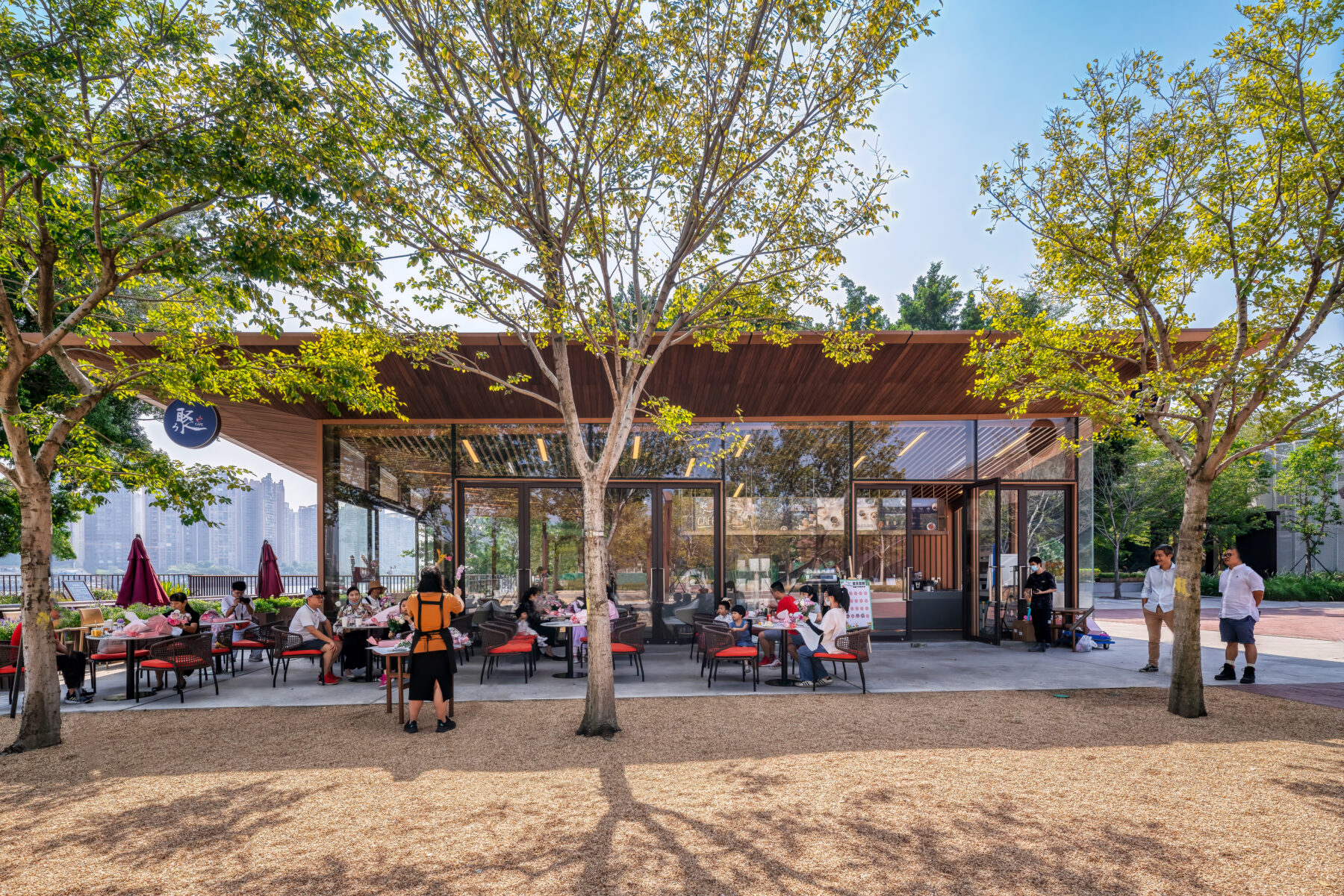Photo of the new cafe building with people sitting at tables and view of the waterfront and city in the periphery.