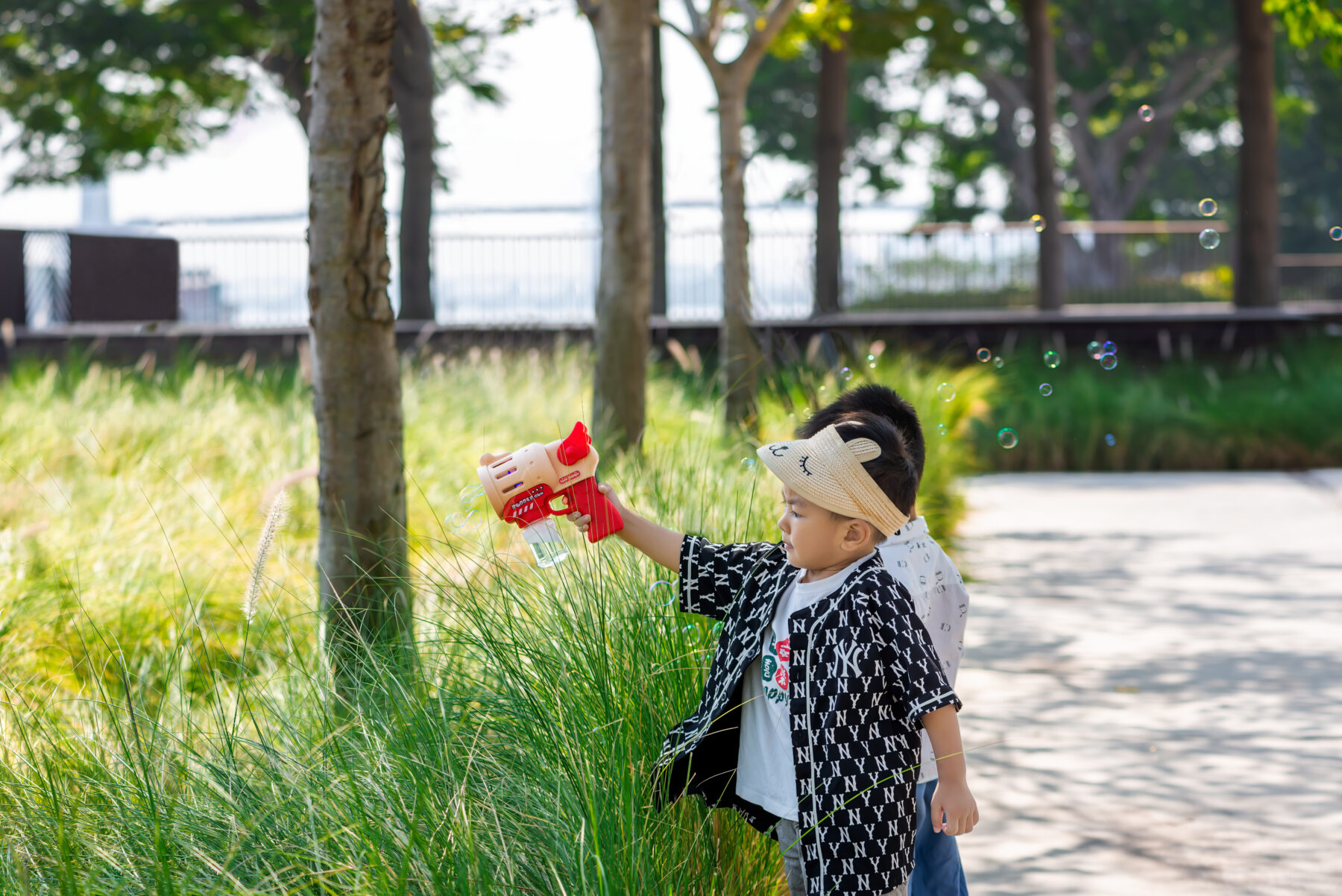 photography of small children playing with bubbles along the tree-lined pathway with tall grass