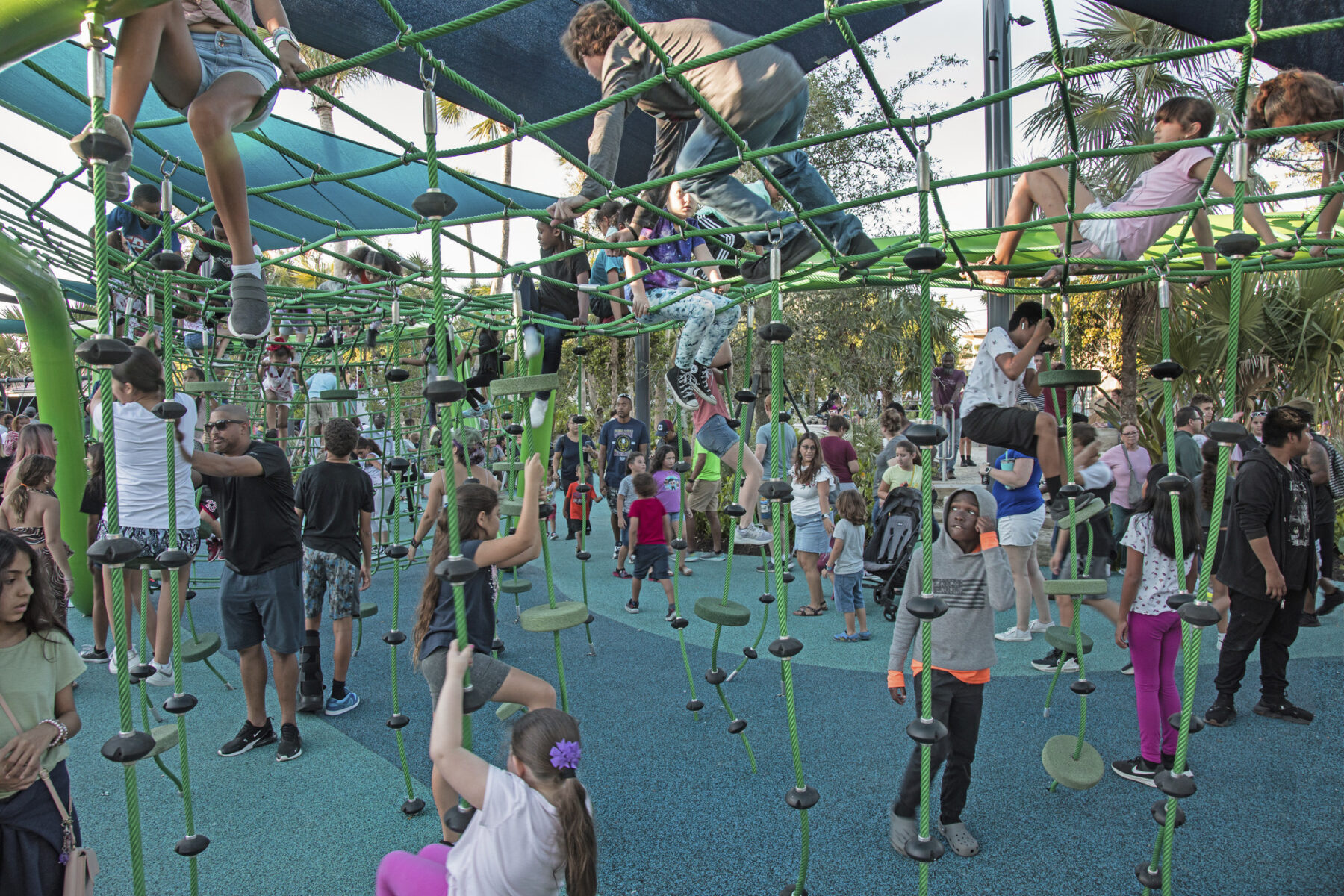 Dozens of children hang from and climb atop a rope play structure, looking out across the park