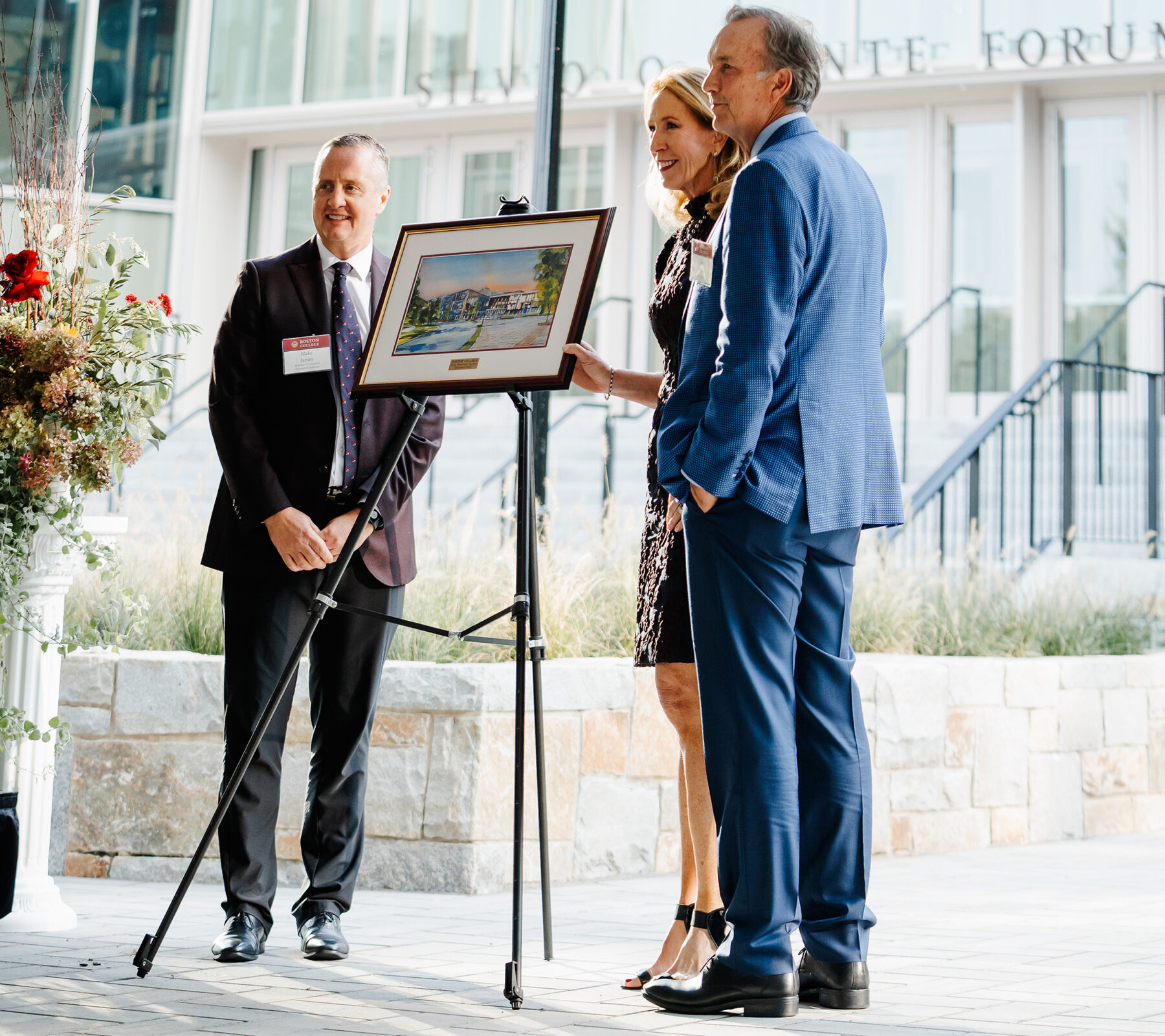 three people pose with a framed painting of the new facility