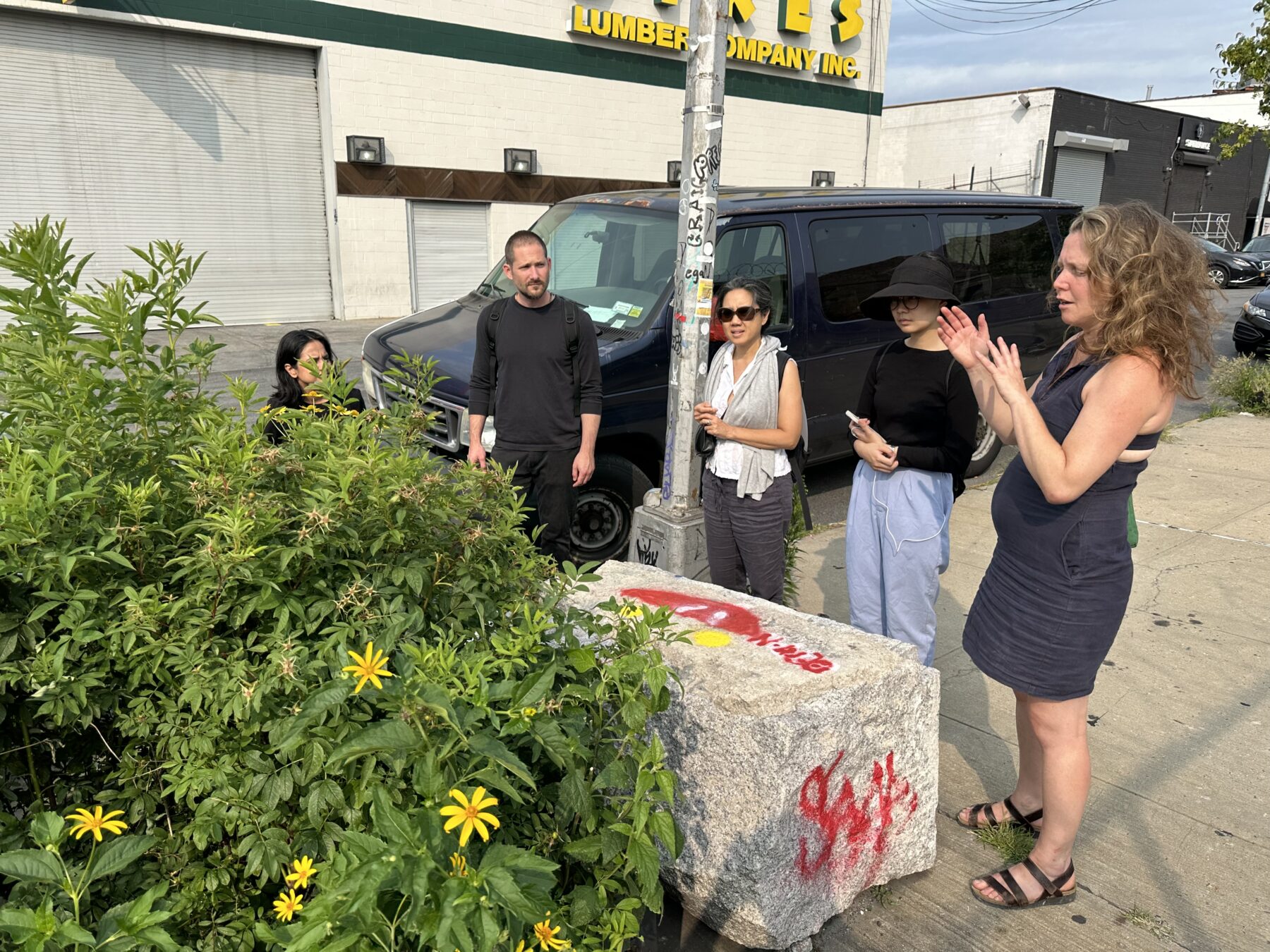 small group stands on city street looking at foliage bounded by granite block