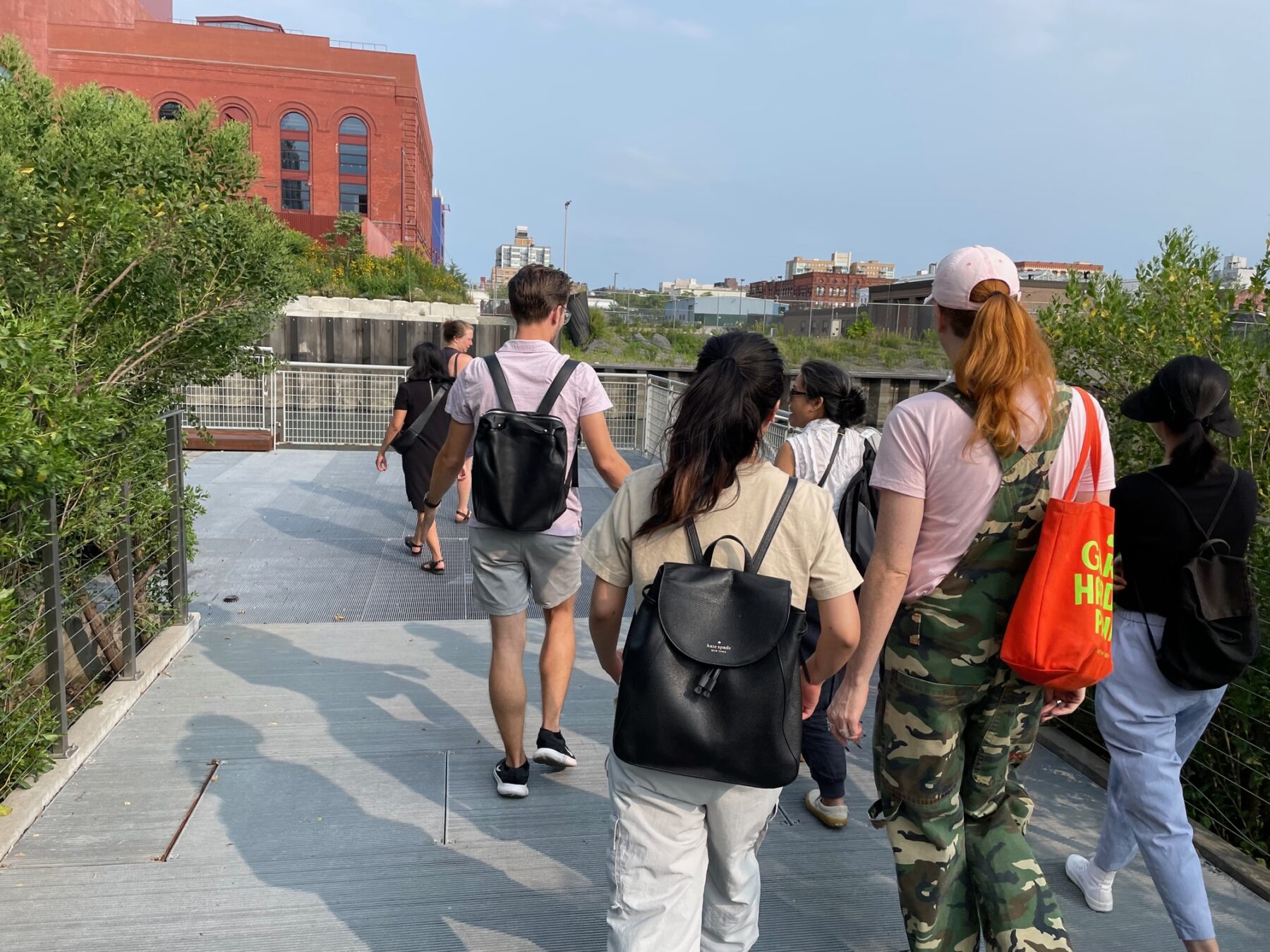 small group in hats and backpacks crosses a pedestrian bridge
