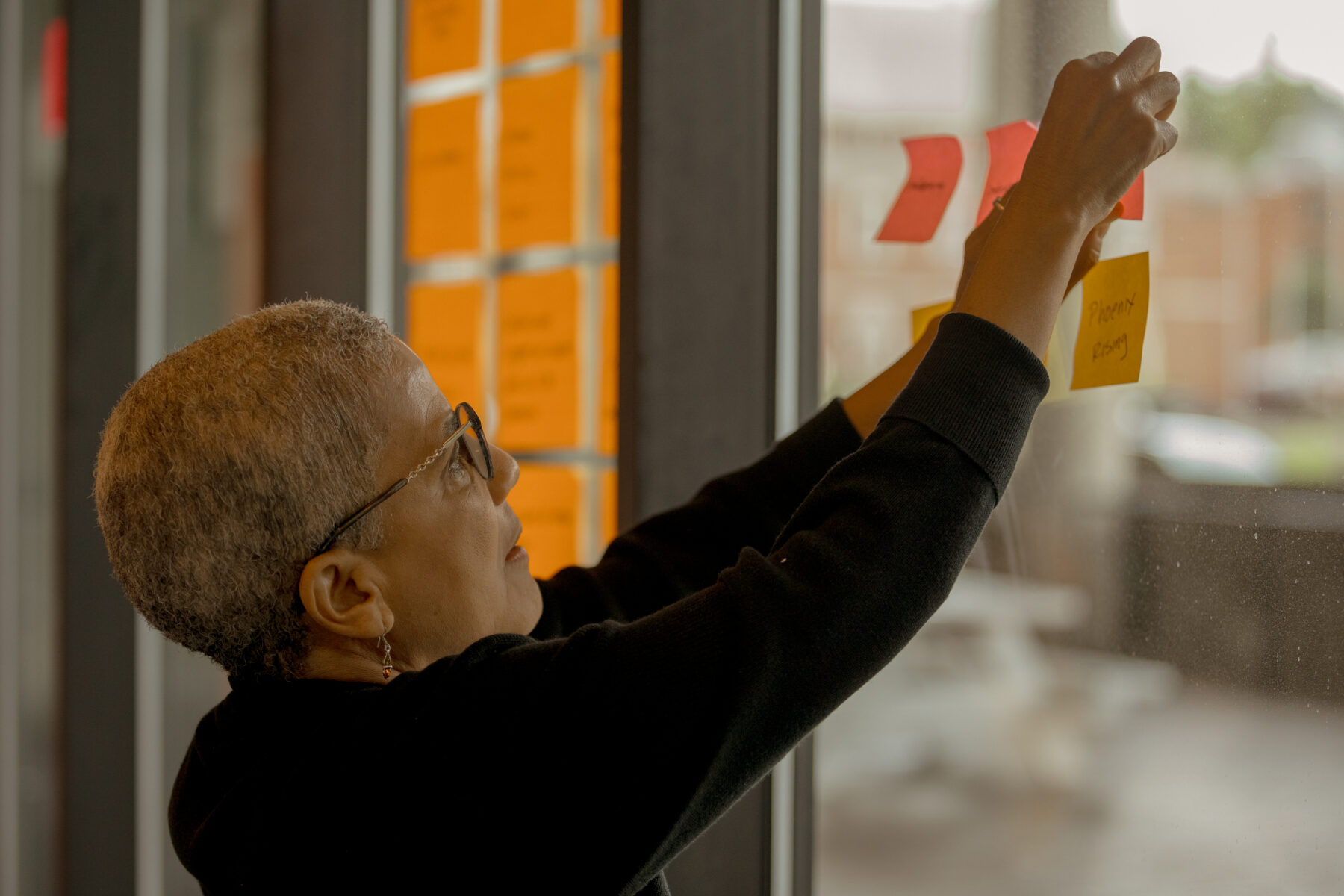 A woman posts a sticky note to a wall that has other colorful sticky notes on it