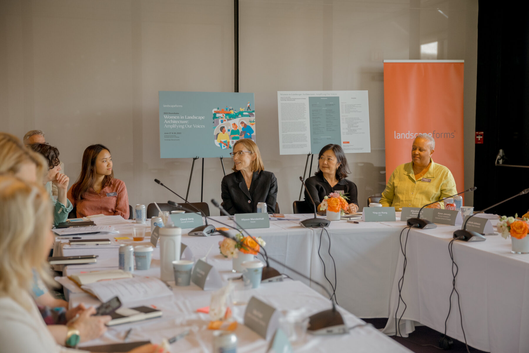 A group of women sit around a table, talking, with microphones