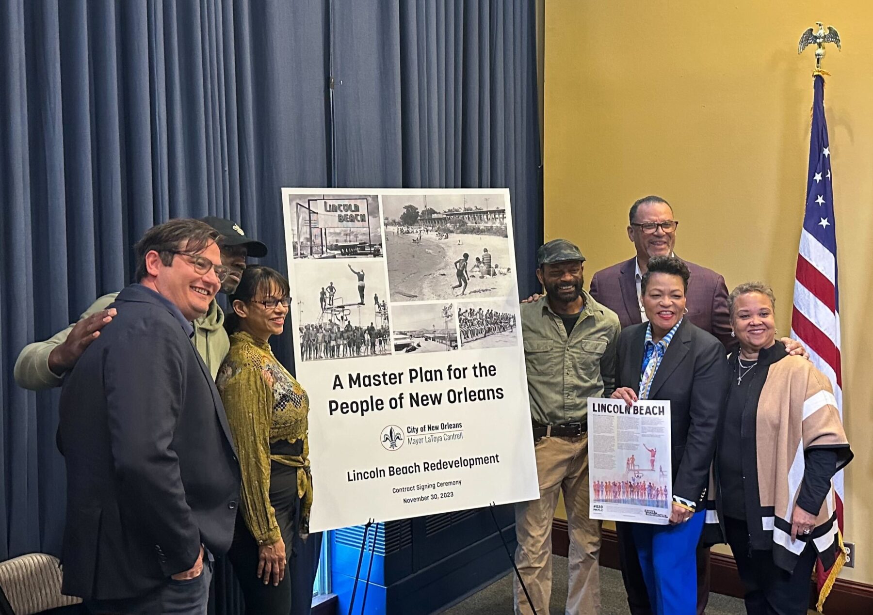 a group of people smiling standing around a poster that says a master plan for the people of new orleans