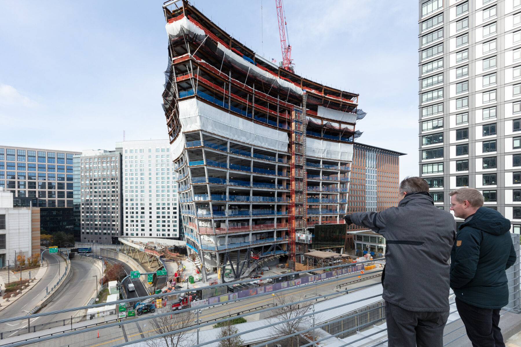 Two men stand above the highway, pointing across the roadway to 10 world trade, which is under construction