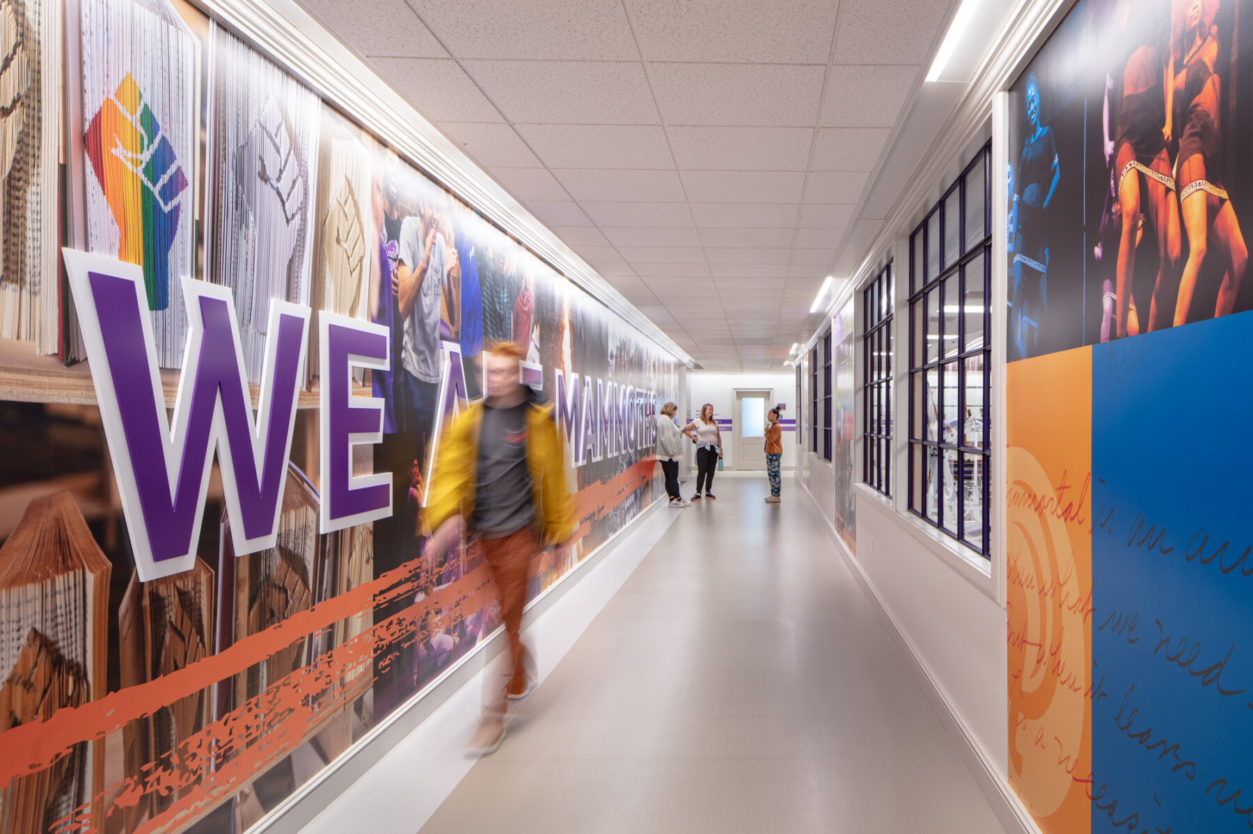 photograph of student walking down main corridor with glass windows on one side and custom graphics on the other