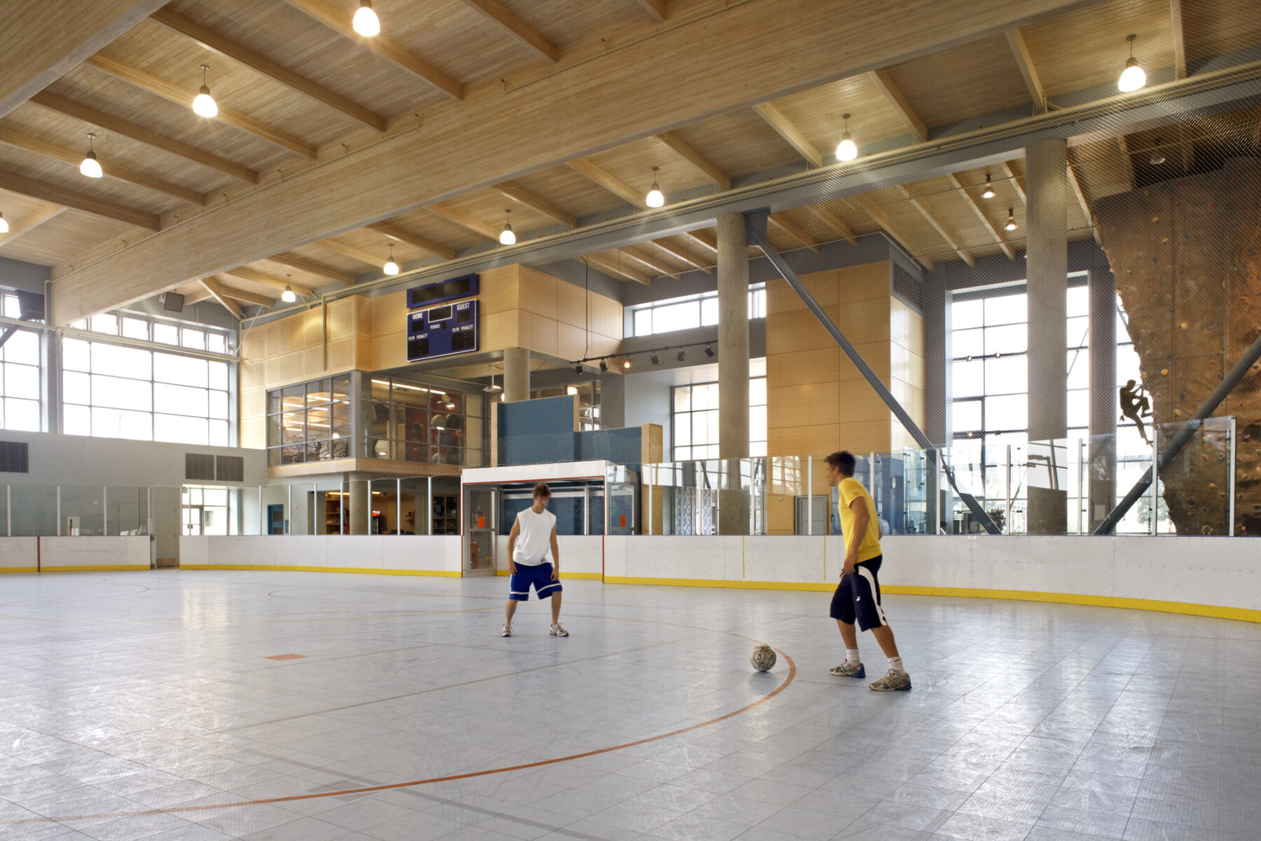 color photo of two young men playing soccer indoors in lofty, timber-paneled rec room