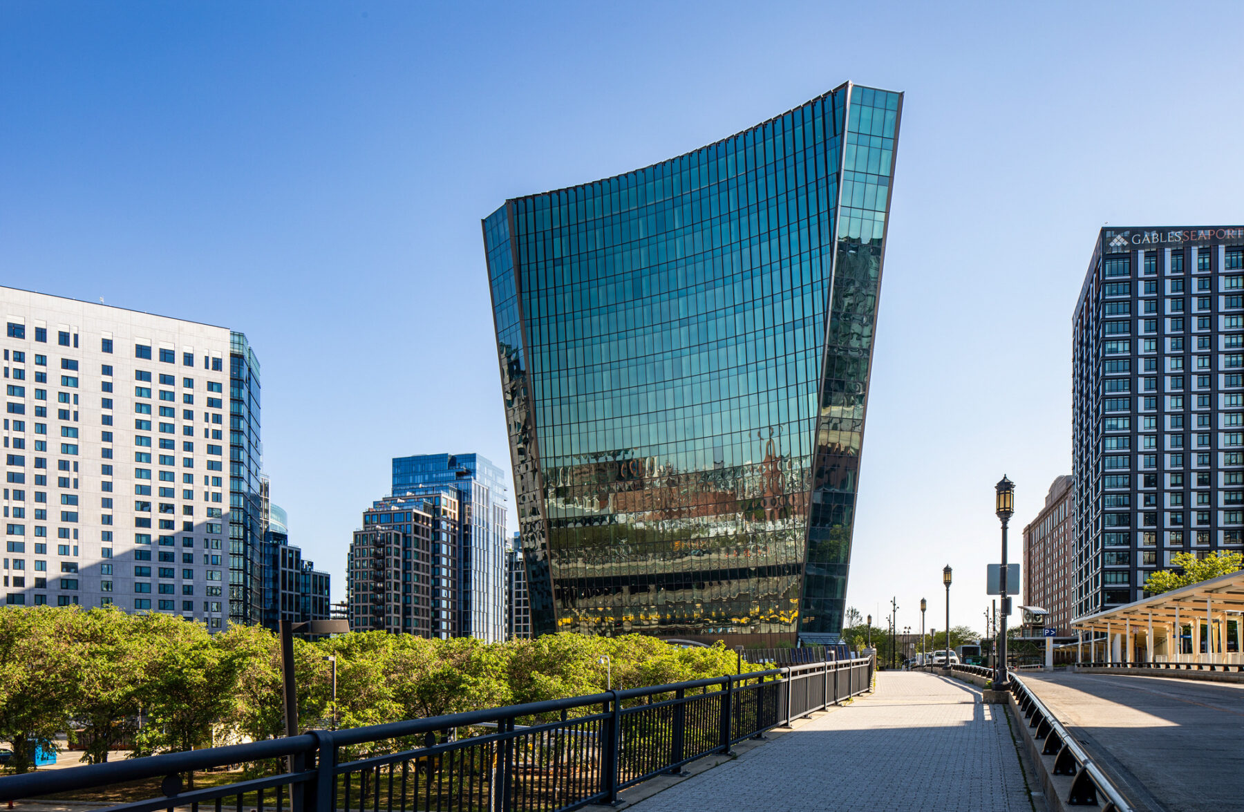 Photo of building from the ground with pedestrian walkway leading up to the glass facade and the building mass extending outwards at the top