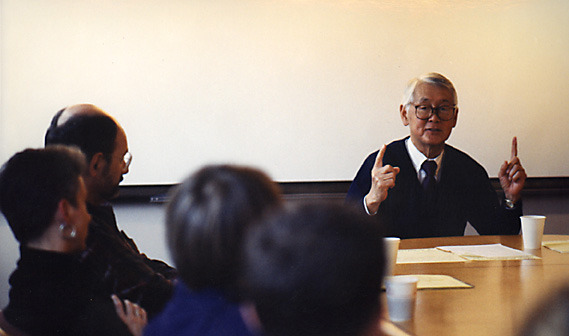 color photo of an older Hideo Sasaki energetically addressing eager a table full of designers