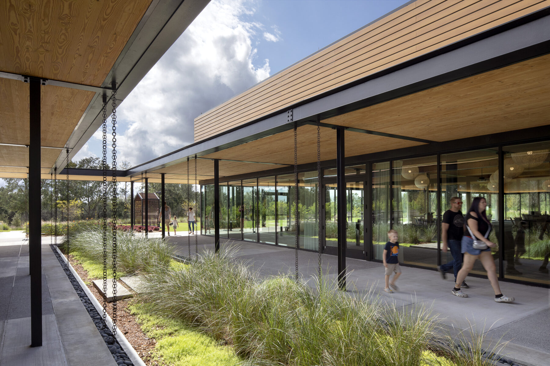 Photo of the water garden courtyard at the Bonnet Springs Park Event Center, showing its row of plantings watered by rain chains hanging from the Center's cross-laminated timber roof canopy.