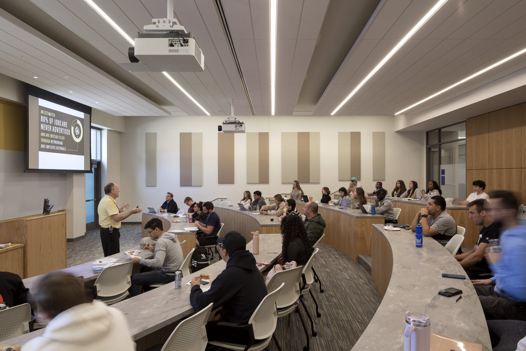 Photo of case study classroom with faculty standing at front of the projector screen and students gathered for class