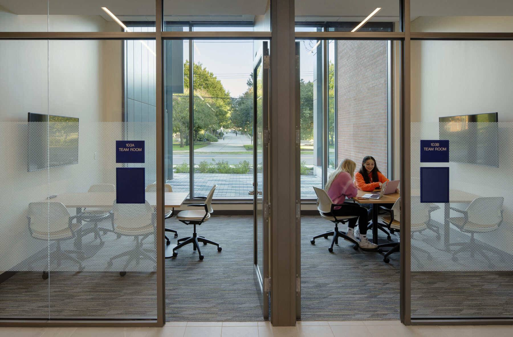 Photo with view into ground floor study rooms with full height windows viewing the pedestrian walkway through campus on the exterior