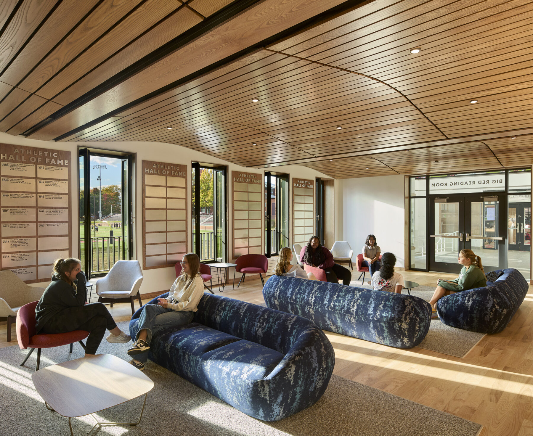Inside the donor lounge, the curved wooden ceiling profile frames the space with views outside the windows to the football field.