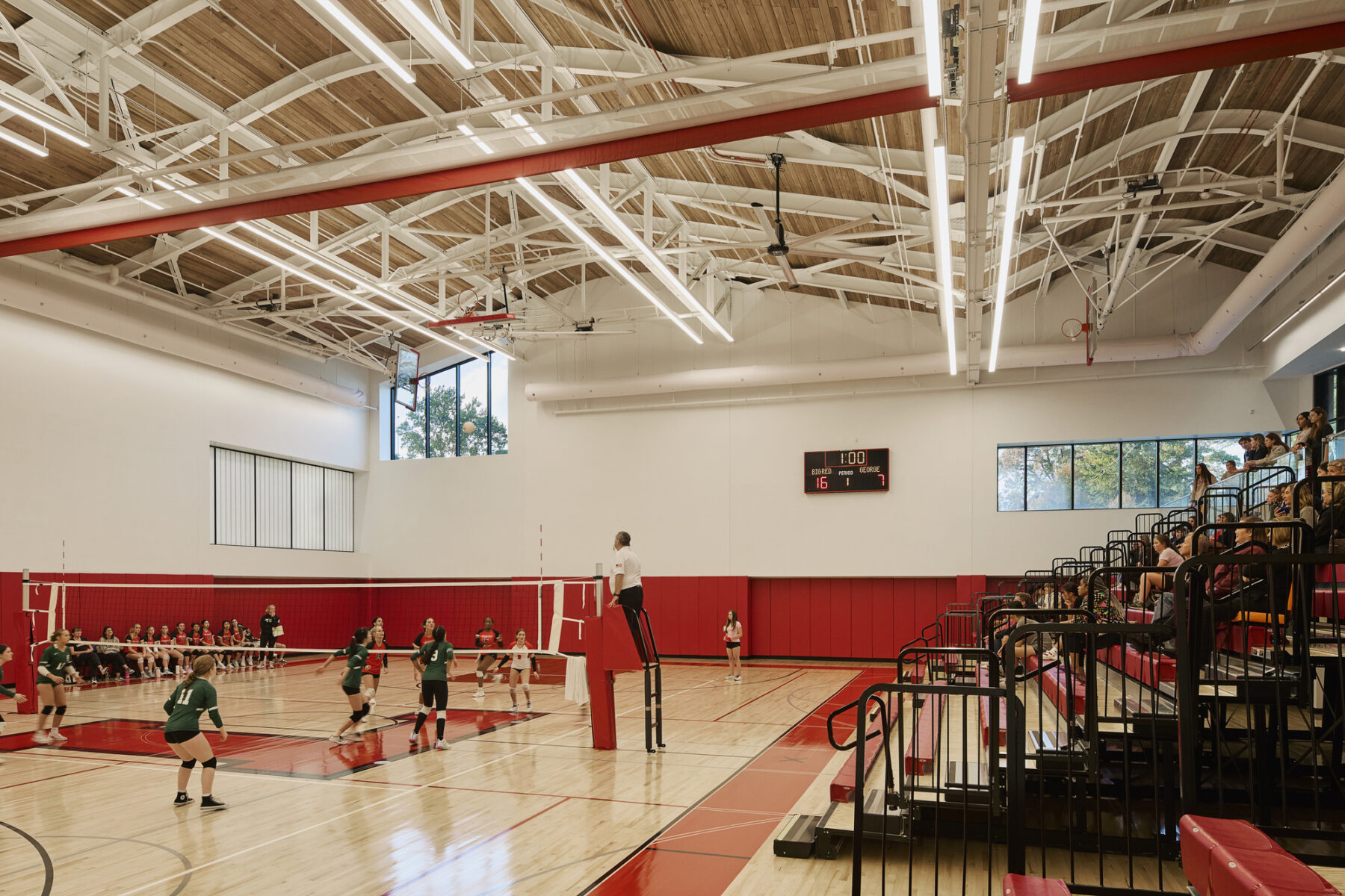 The interior of the new gymnasium with it's large volume, curved, wooden ceiling, and volleyball practice on the court