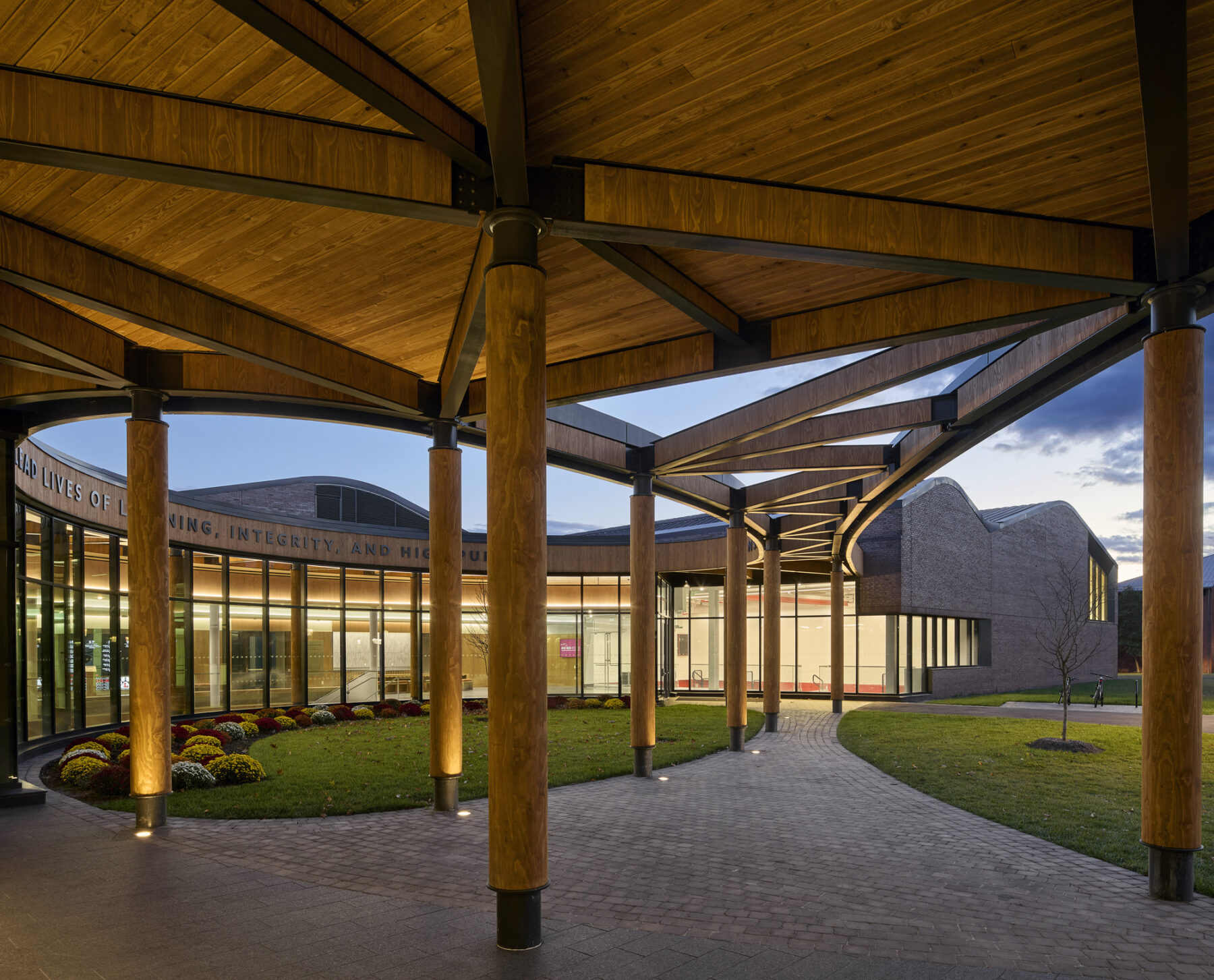 Photo taken beneath the wooden overhang of the Harkness Courtyard, taken at dusk with the glowing light spilling out from the windows creating a welcoming entry.