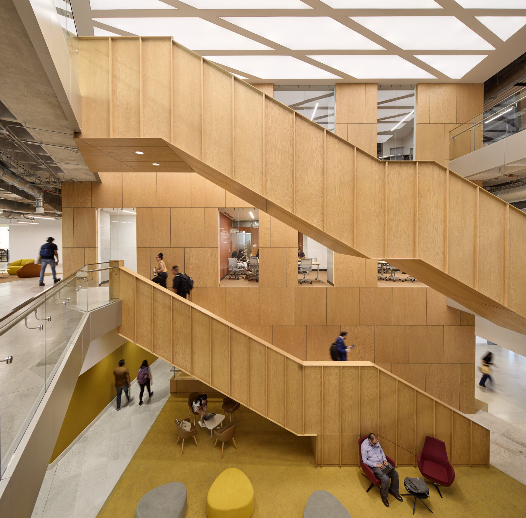 Interior photo taken from the second level looking across at the wooden staircases and windows into meeting spaces