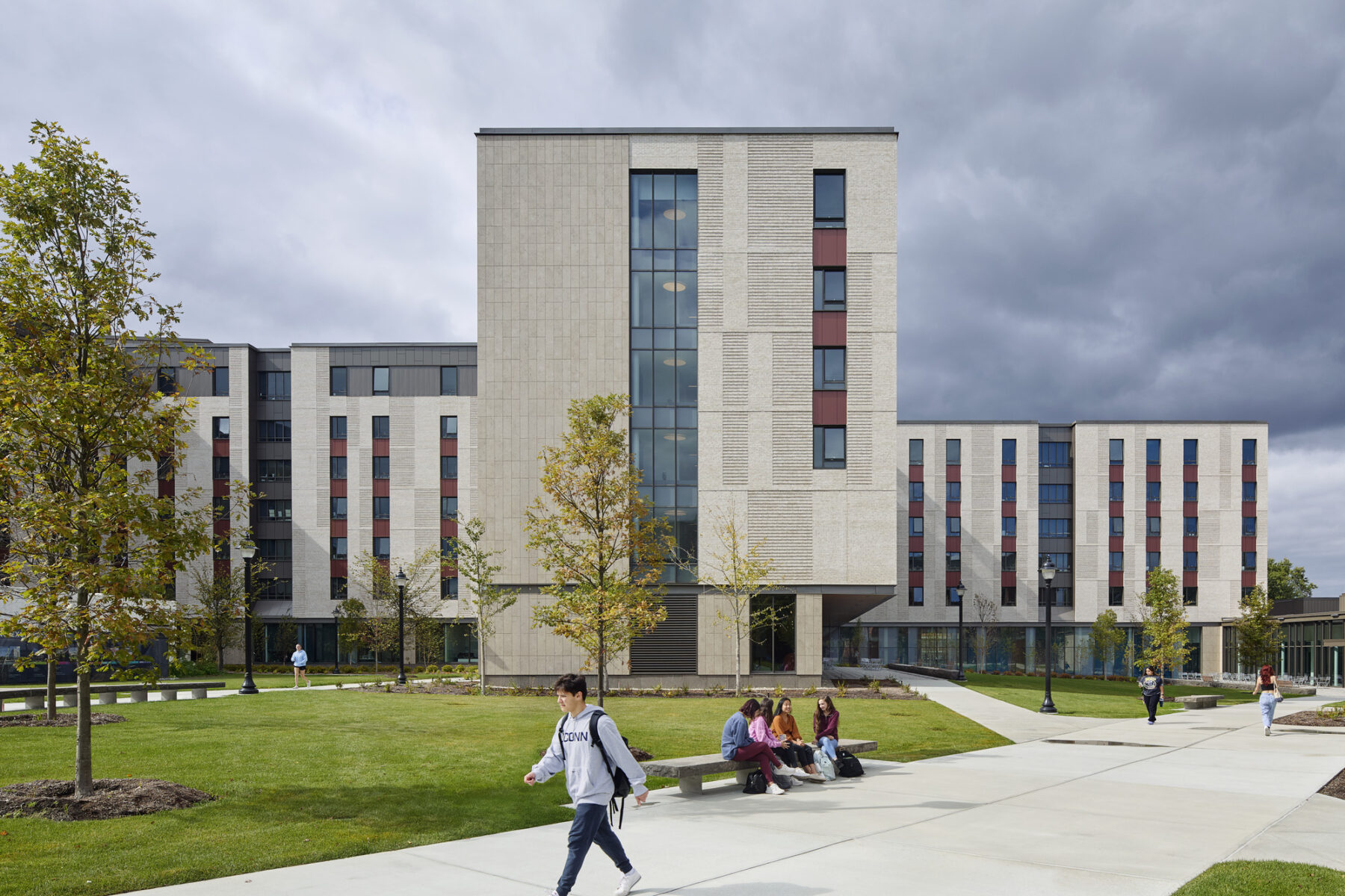 Photo of building exterior facing the two quads split by the building mass with pedestrian pathways in the foreground and students sitting on a bench