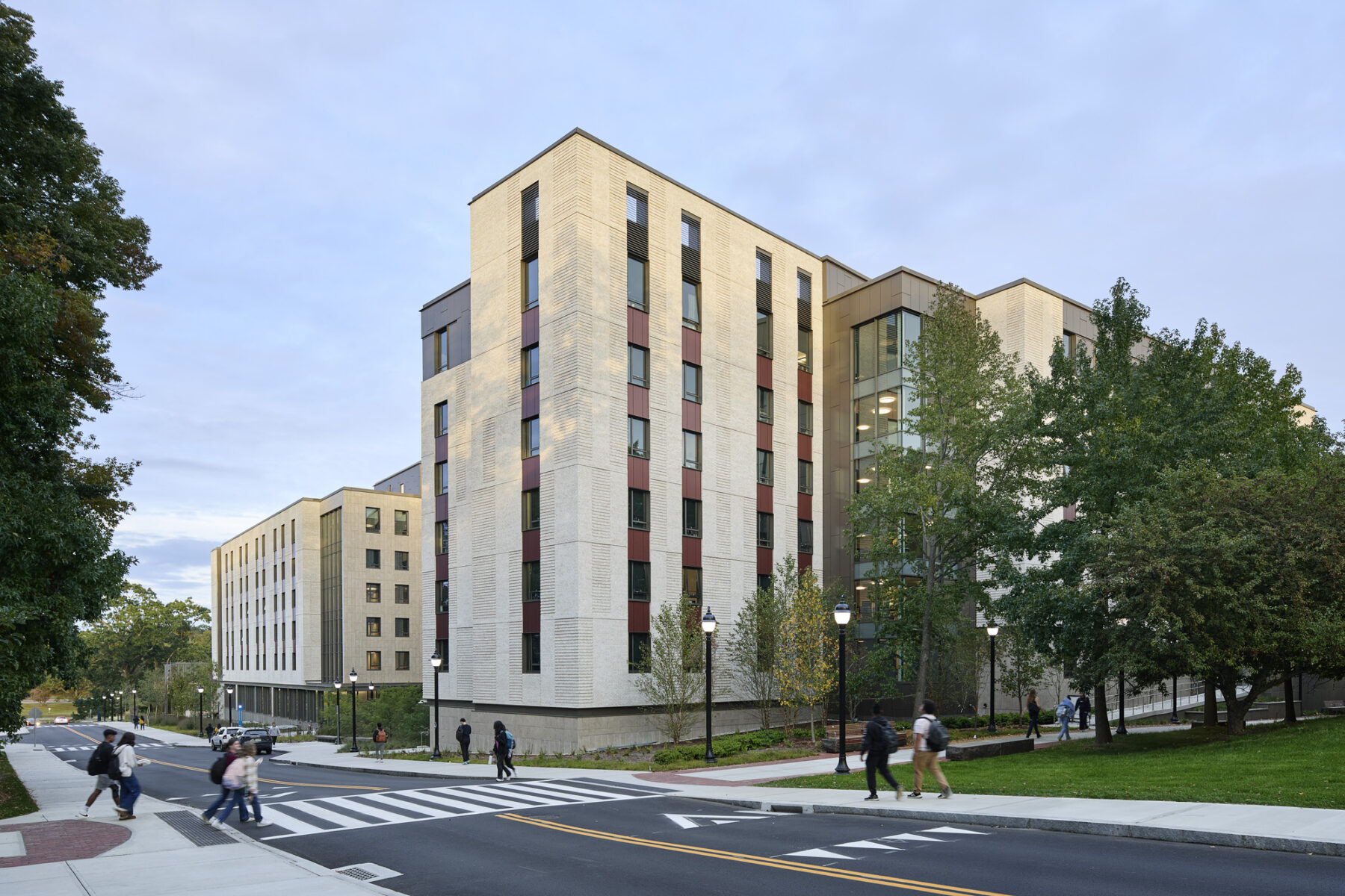 Exterior photo looking down Gilbert Road at crosswalk with view of building facade and pedestrians crossing the street on Academic Way
