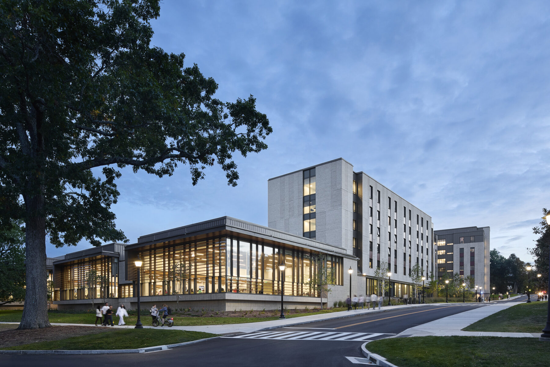 Dusk photo viewing the dining and residence hall from across the street with interiors glowing with light