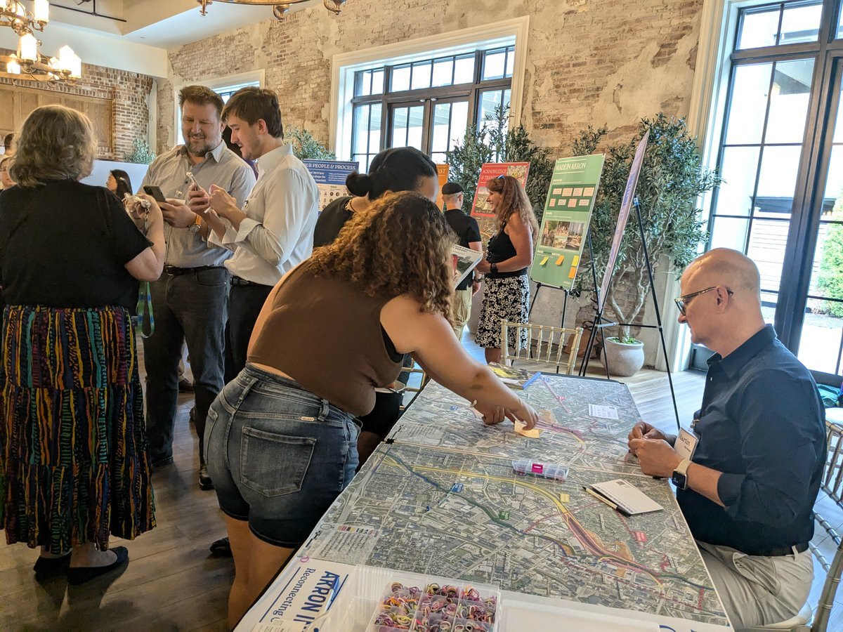 Photo of community engagement session with Sasaki principal Martin Zogran sitting behind a table with maps and diagrams, and community members looking and adding sticky notes to the map