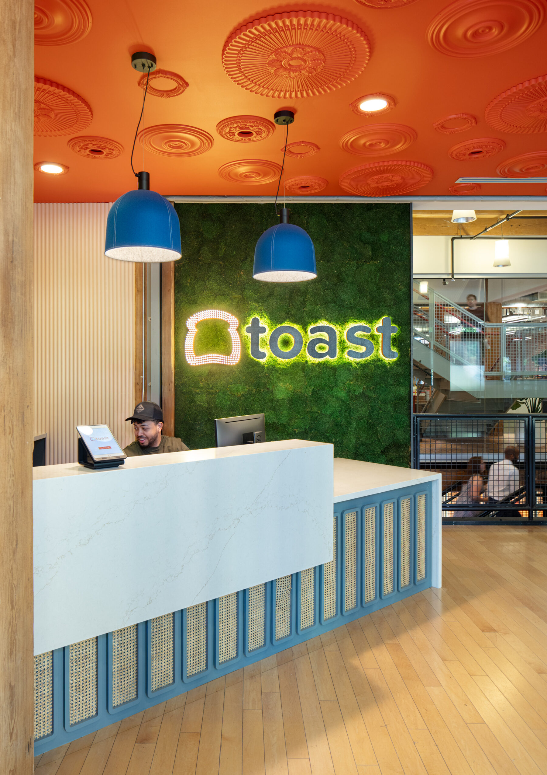photograph of reception desk, featuring backlit fixture of Toast logo on a living green wall