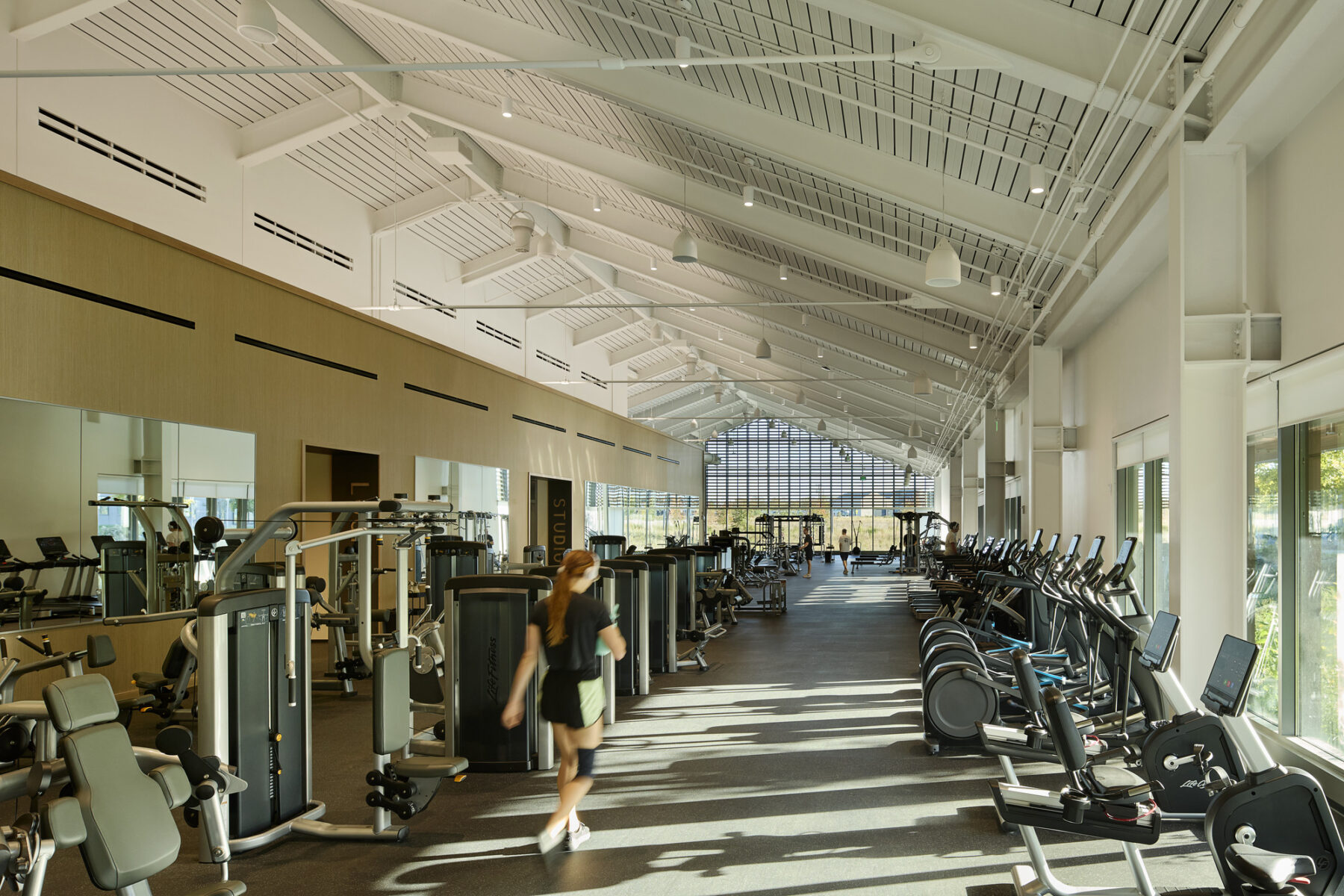 Photo of large open fitness area with machines along the walls and large windows with views out