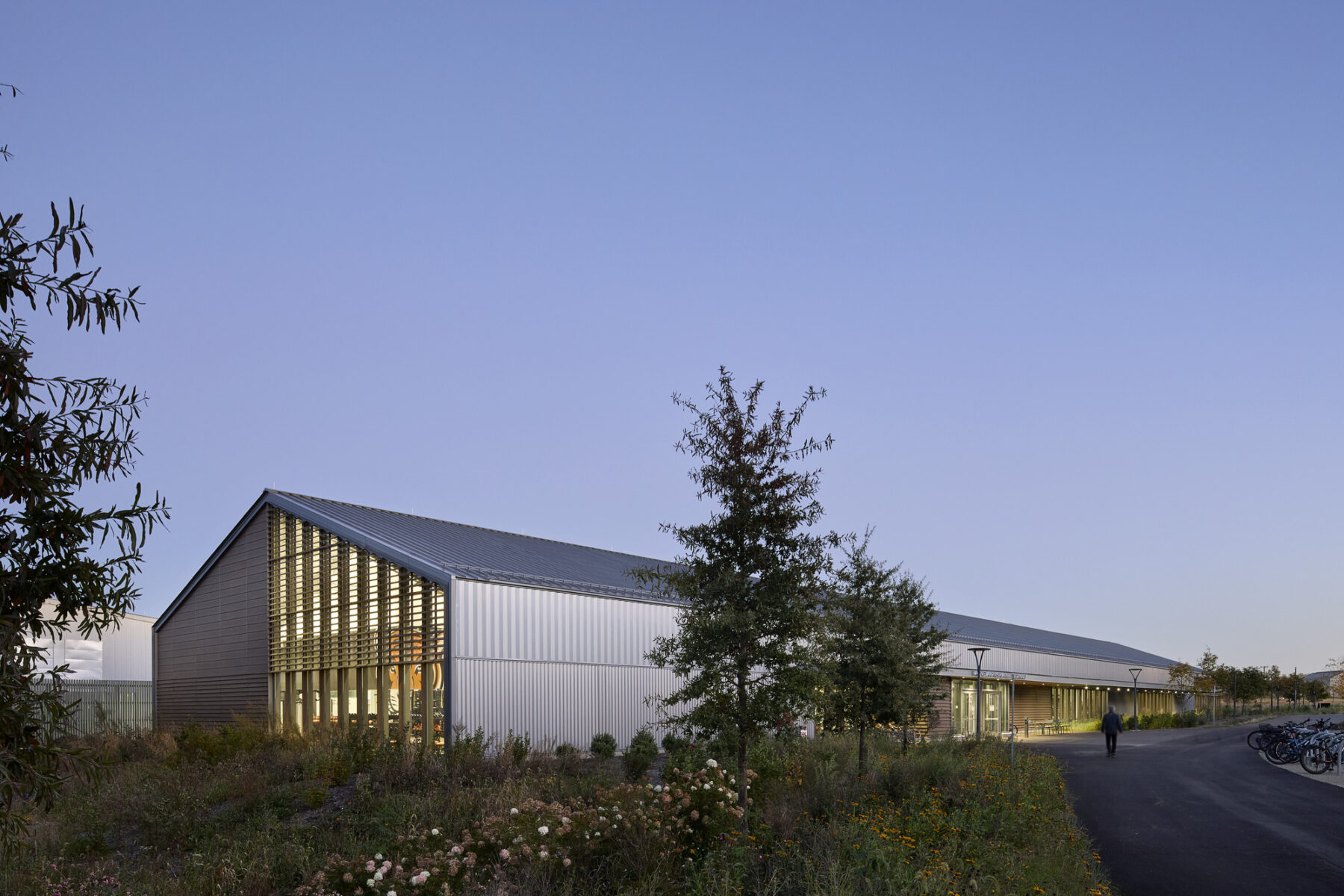 Dusk photo of exterior, main entry with views inside, bike racks and connecting pedestrian paths