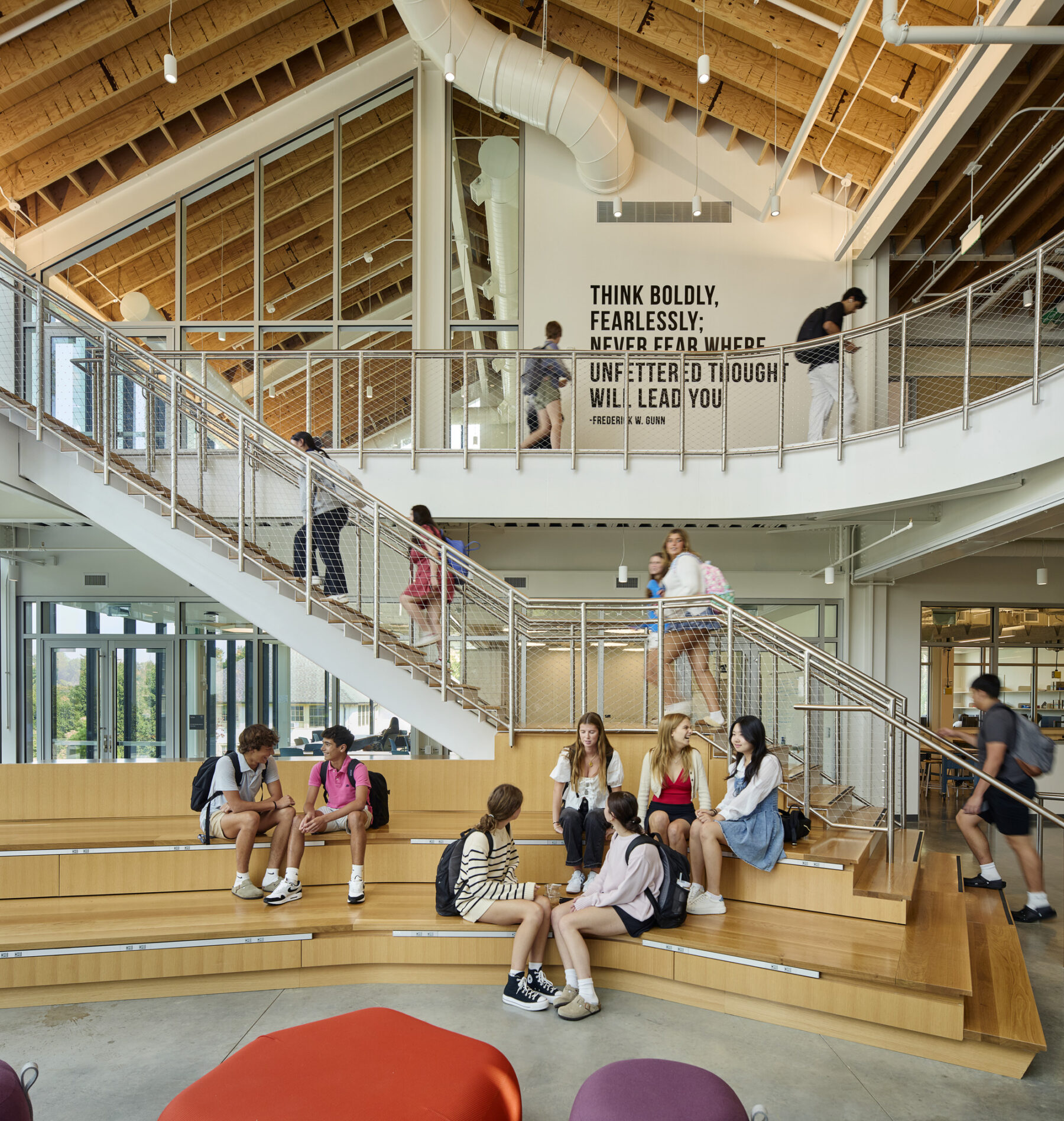 Interior photograph with staircase, custom wood benches and students sitting and socializing
