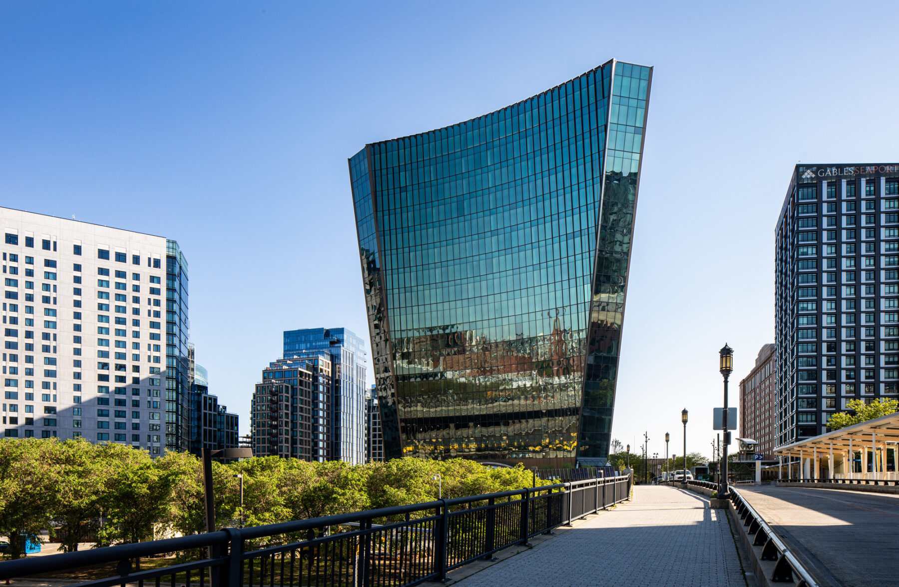 View of glass building in city surrounded by other high rise buildings.
