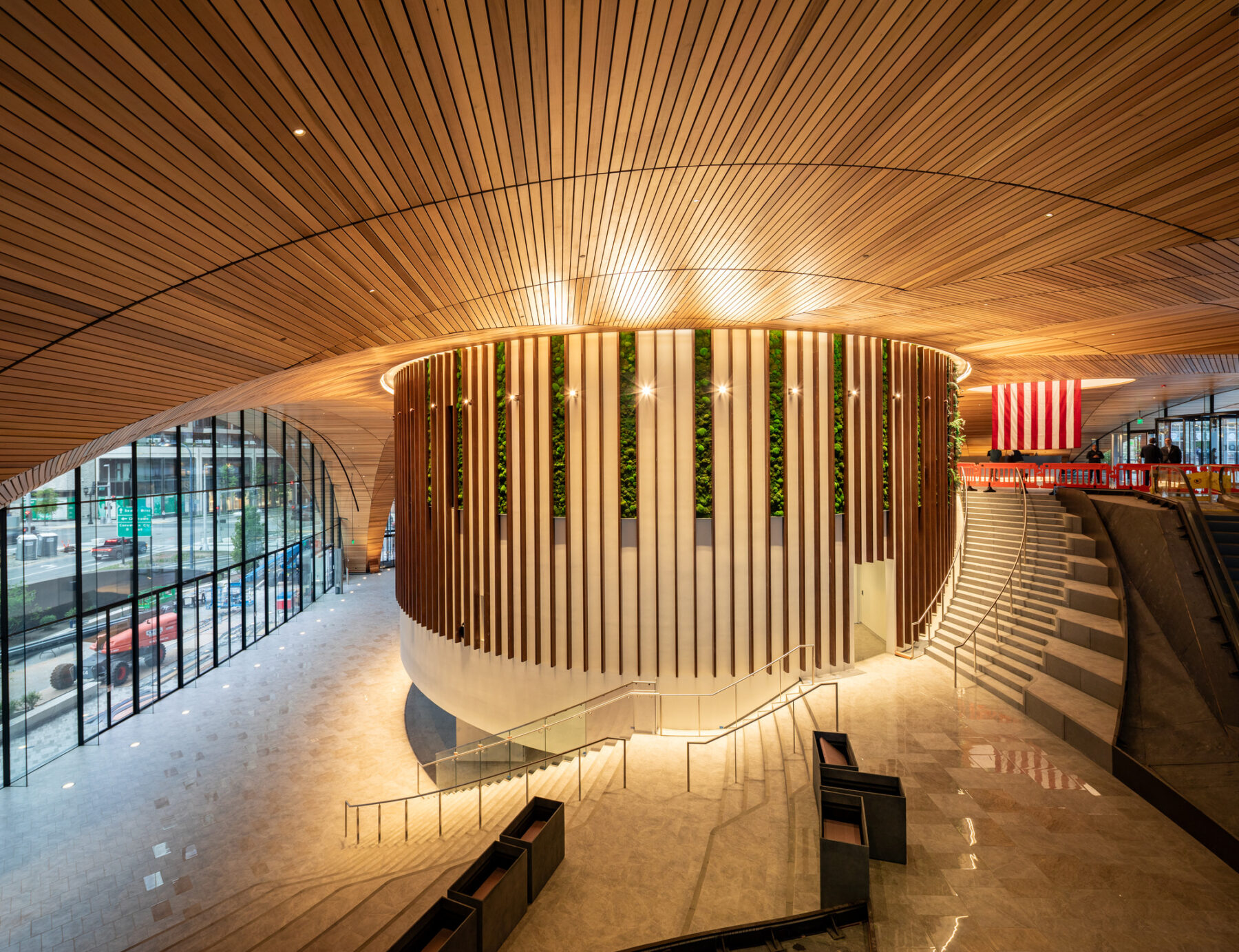 Interior lobby of office building with wood ceilings and glass doors. The center of the photo shows a sweeping staircase.