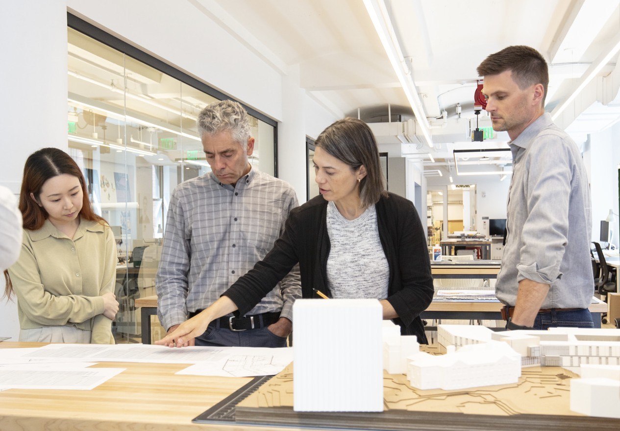 A group of people gather around a large table, looking at an architectural model