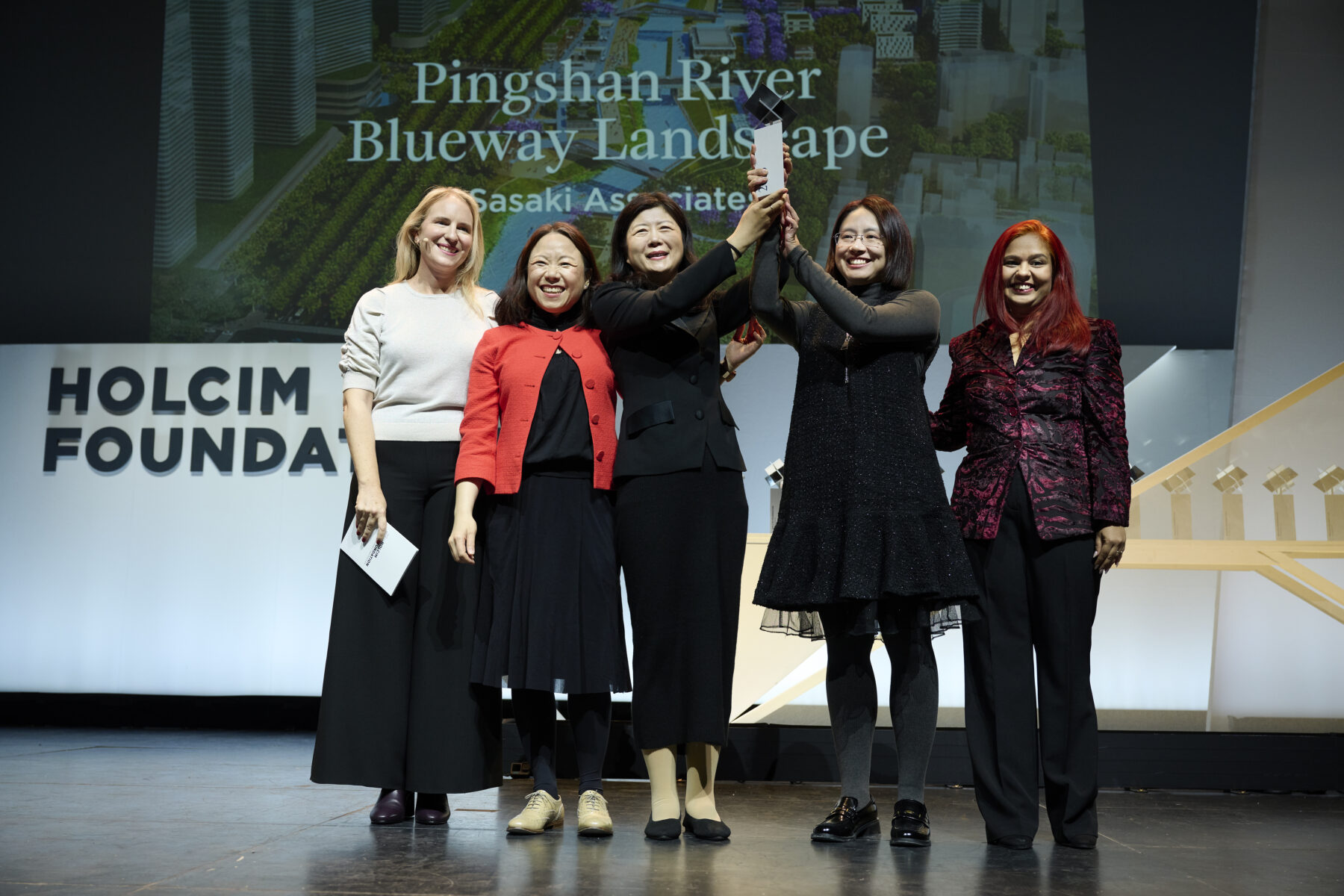 Photo from the awards ceremony with Sasaki designers holding up award on stage with judges and host standing together and smiling