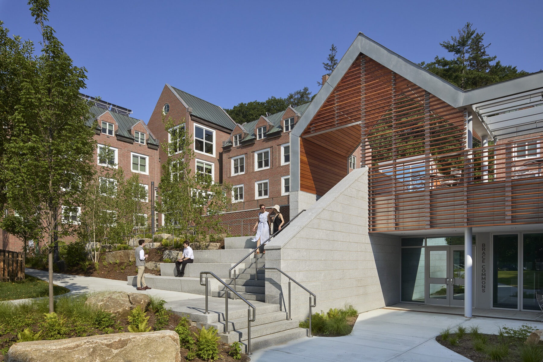 Photo of building exterior facing the new Brace Commons entry from the mini quad with stairs leading up to pavilion and courtyard above the Commons main door and glass wall beneath