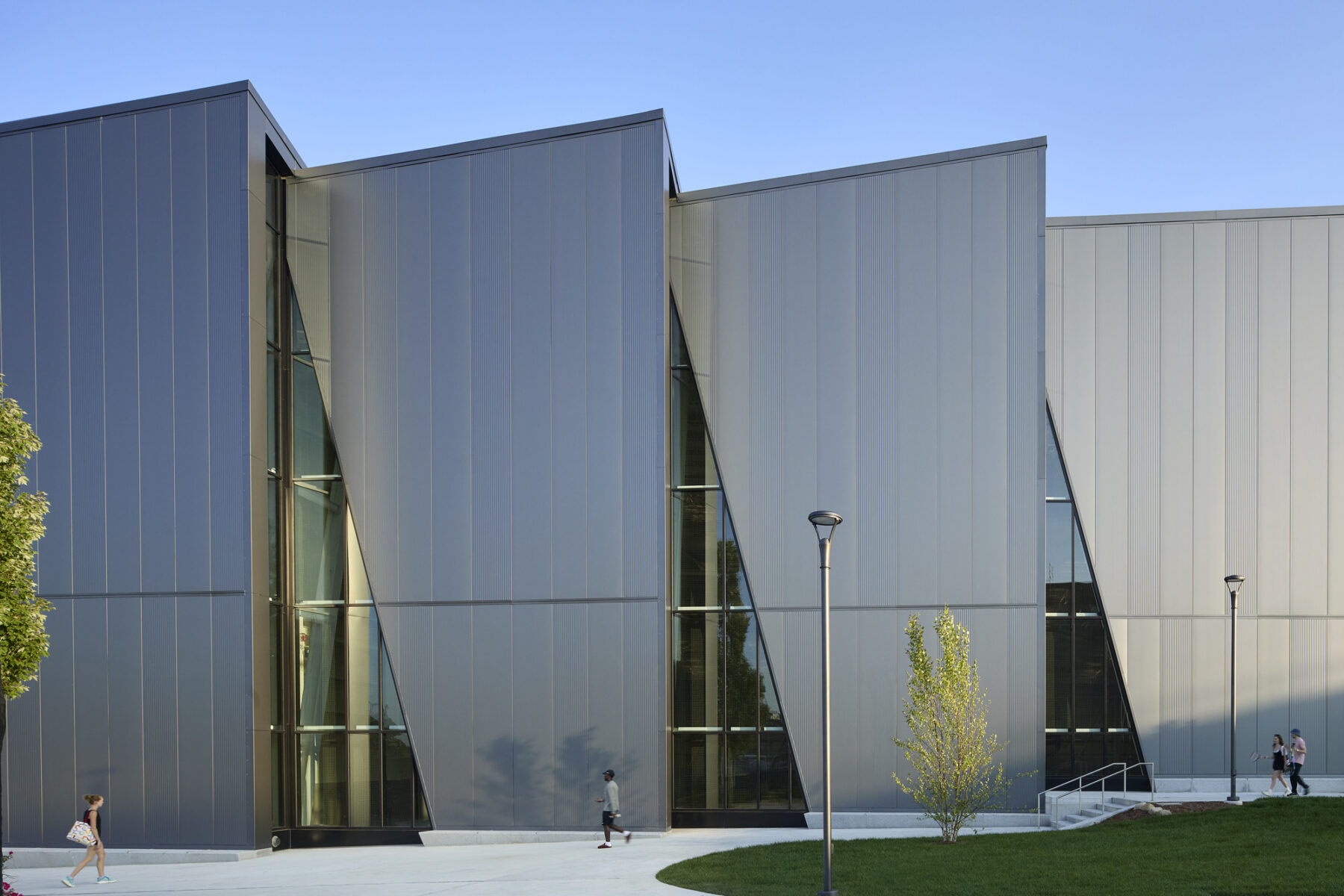 Elevational photograph of the north, saw tooth shaped facade with raking light across the metal panels and large triangle shaped windows