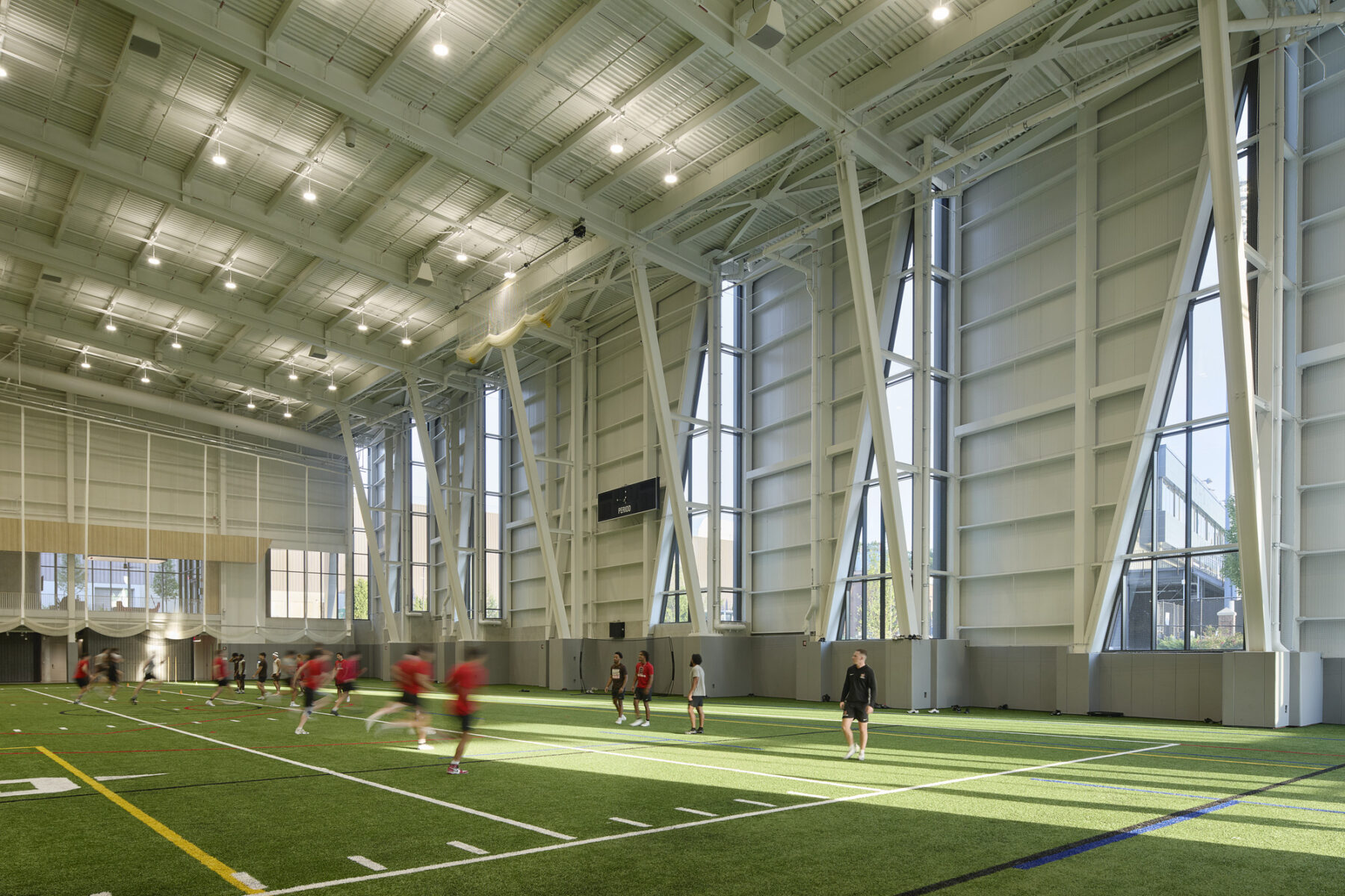 Interior photo with diagonal view of turf field facing the large triangle shaped windows on the north facade with natural light streaming inside