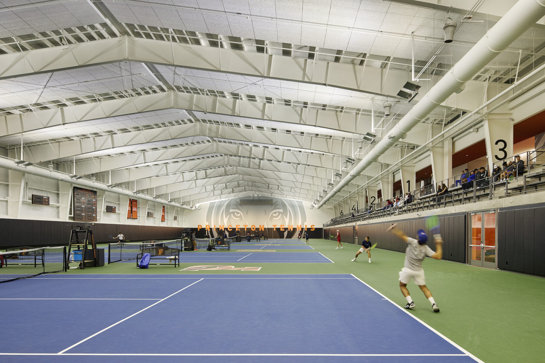 photo of an indoor tennis court with people playing tennis