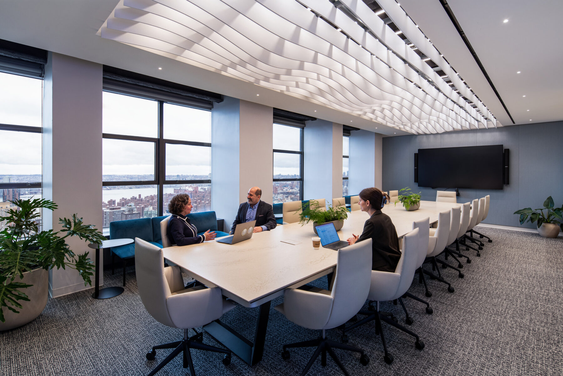 photograph of corporate meeting room with three people gathering on a central table with laptops