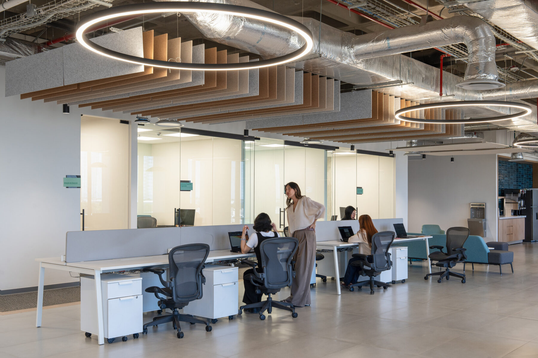 Interior photo of collaborative space with warm tones in the acoustic ceiling panels, desks and concrete floor