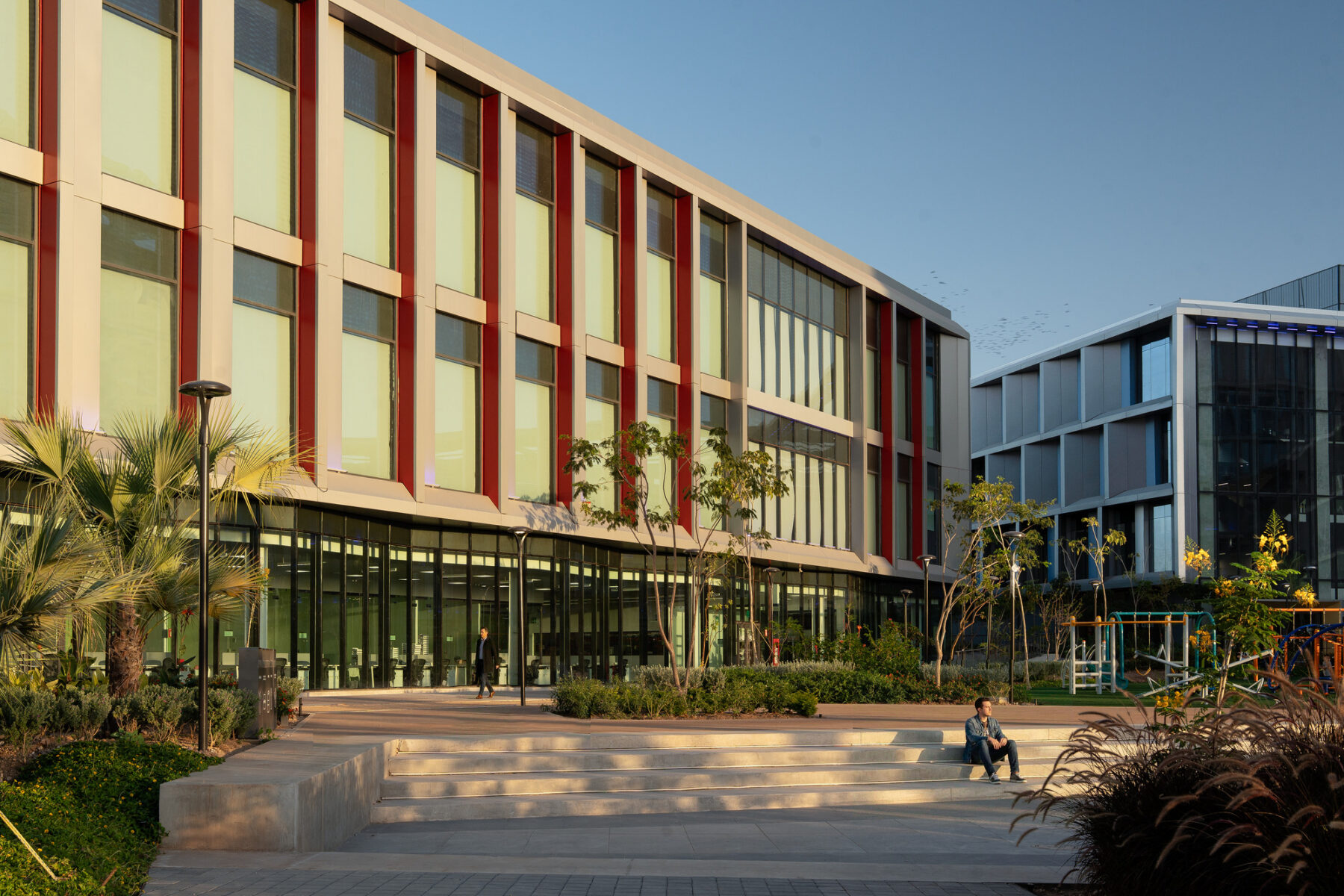 Exterior photo of man sitting on the steps of the plaza in front of laboratory building at sunset