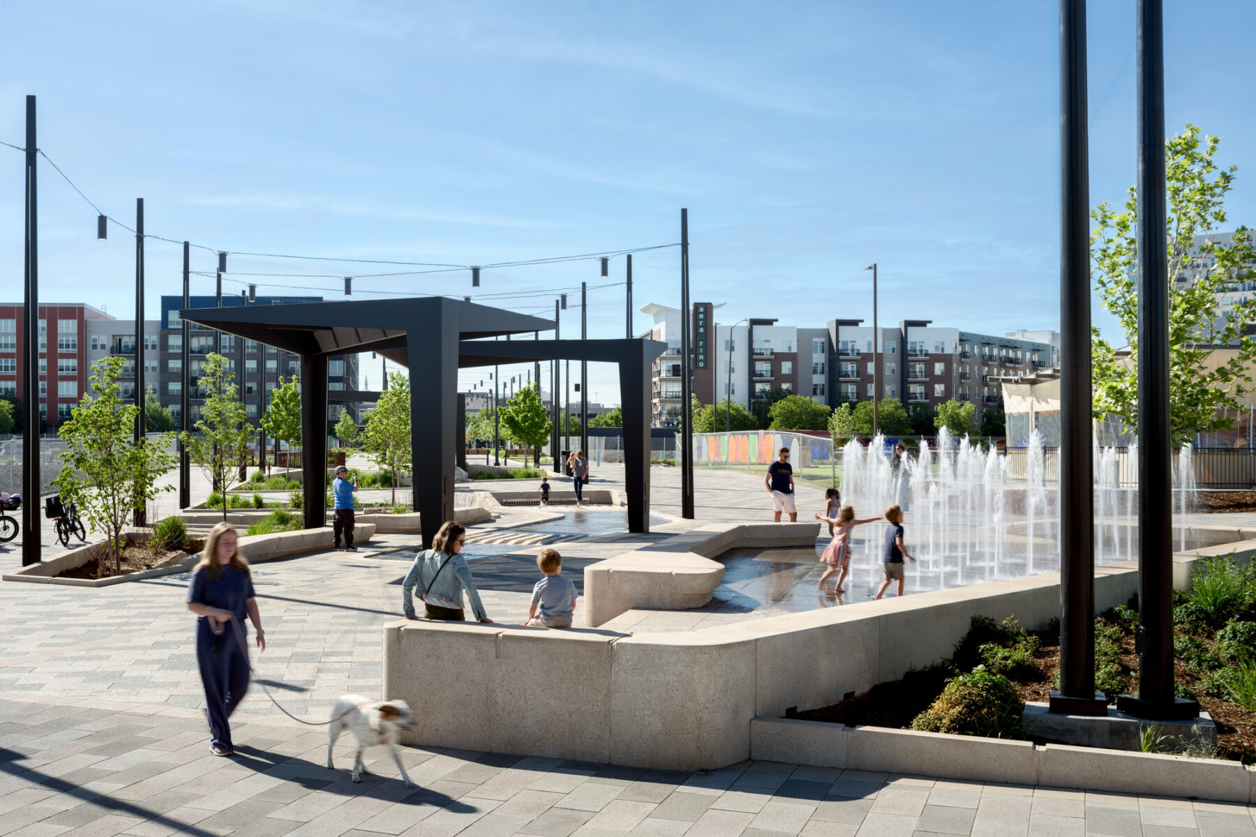 A public plaza with people walking and children playing in a fountain