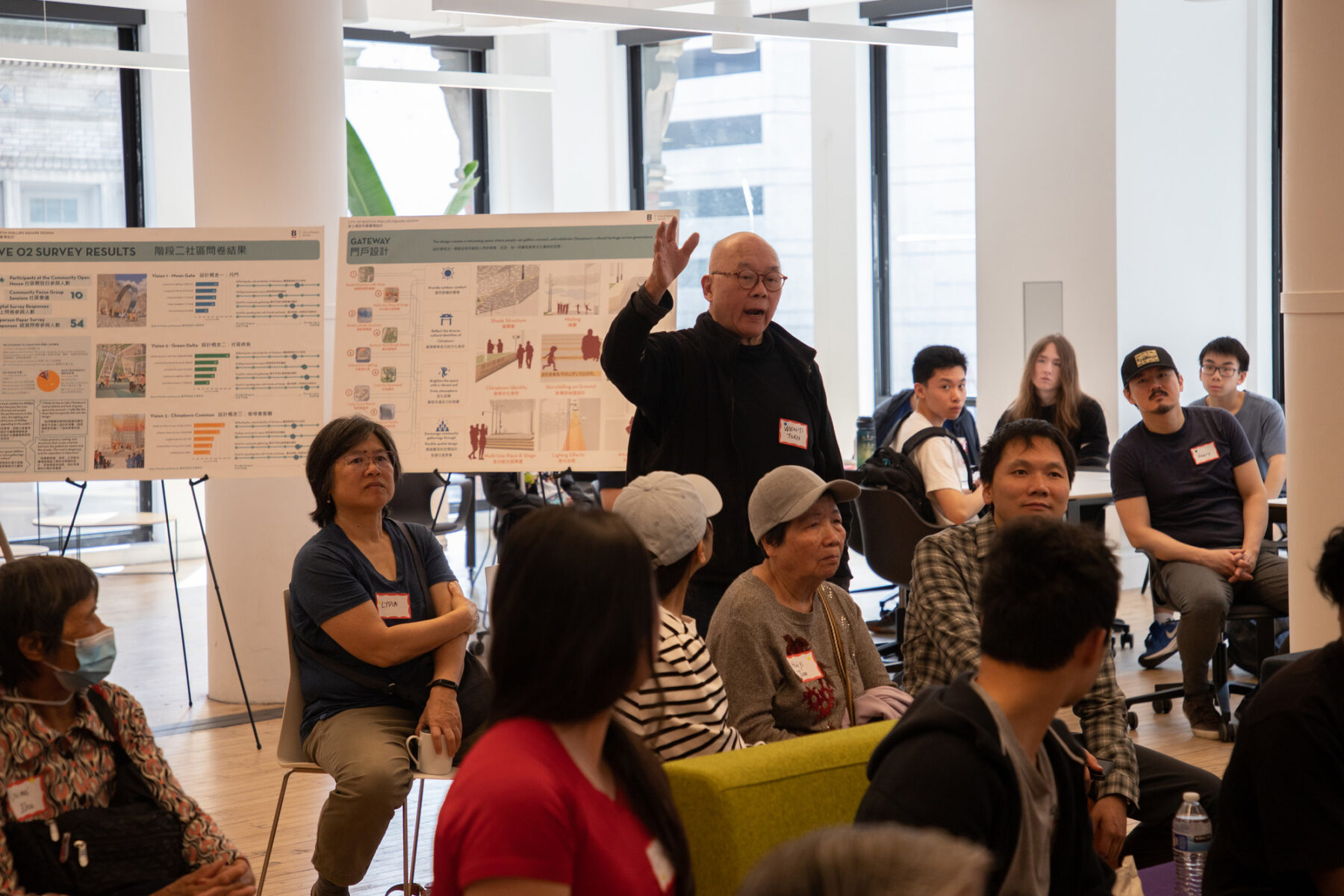 People sitting at a design charrette looking towards a man standing up to raise an opinion
